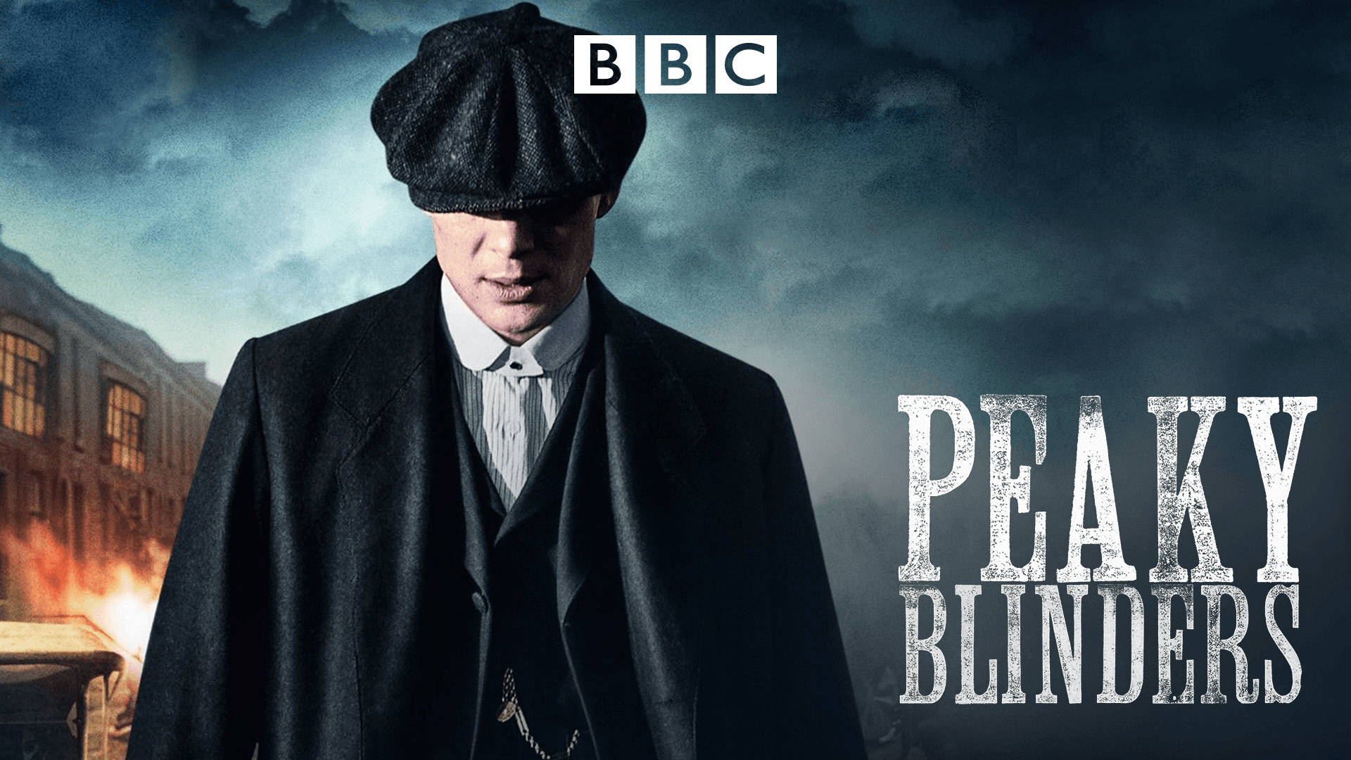 戴平頂帽和外套的男人，在暴風雨天空下，站在燃燒的建築物前。 — Peaky Blinders 壁紙