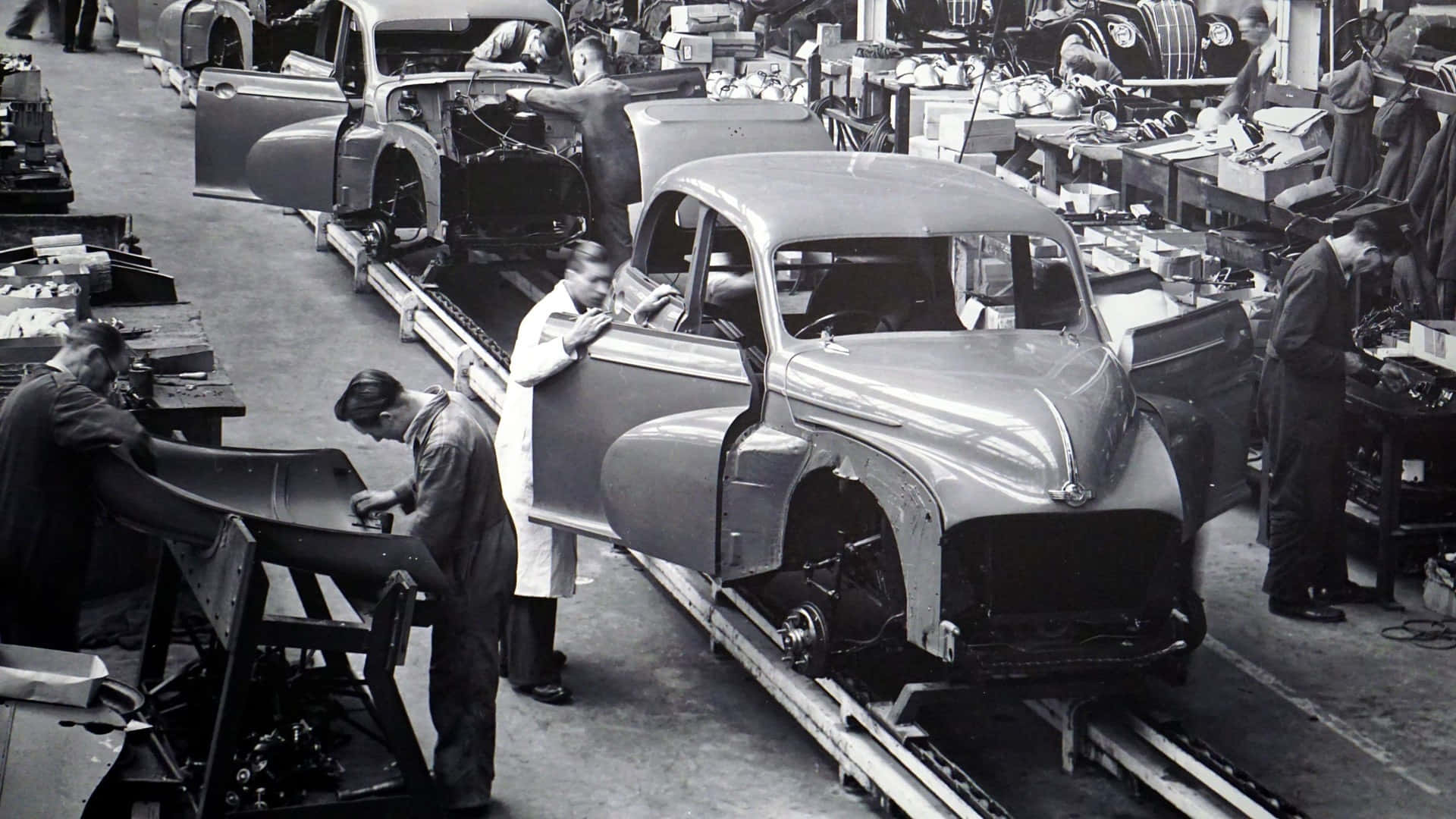 Black And White Vintage Car 桌布 壁紙 — 1940年代服裝的工人在工廠裝配線上組裝復古汽車的黑白照片。