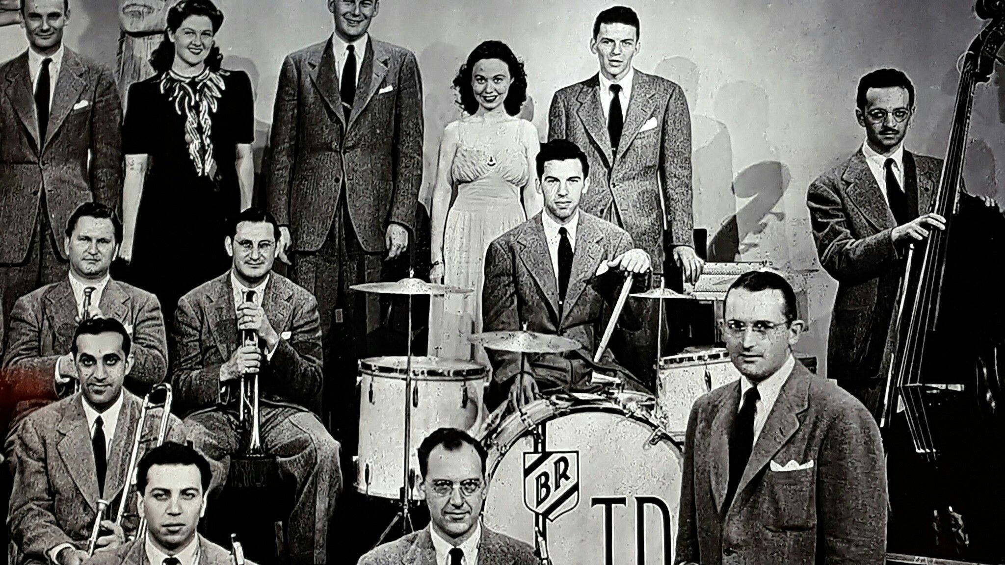 band 桌布 壁紙 — 1940年代爵士樂隊的復古黑白照片，正式擺姿勢，樂器包括鼓、小號和低音提琴。