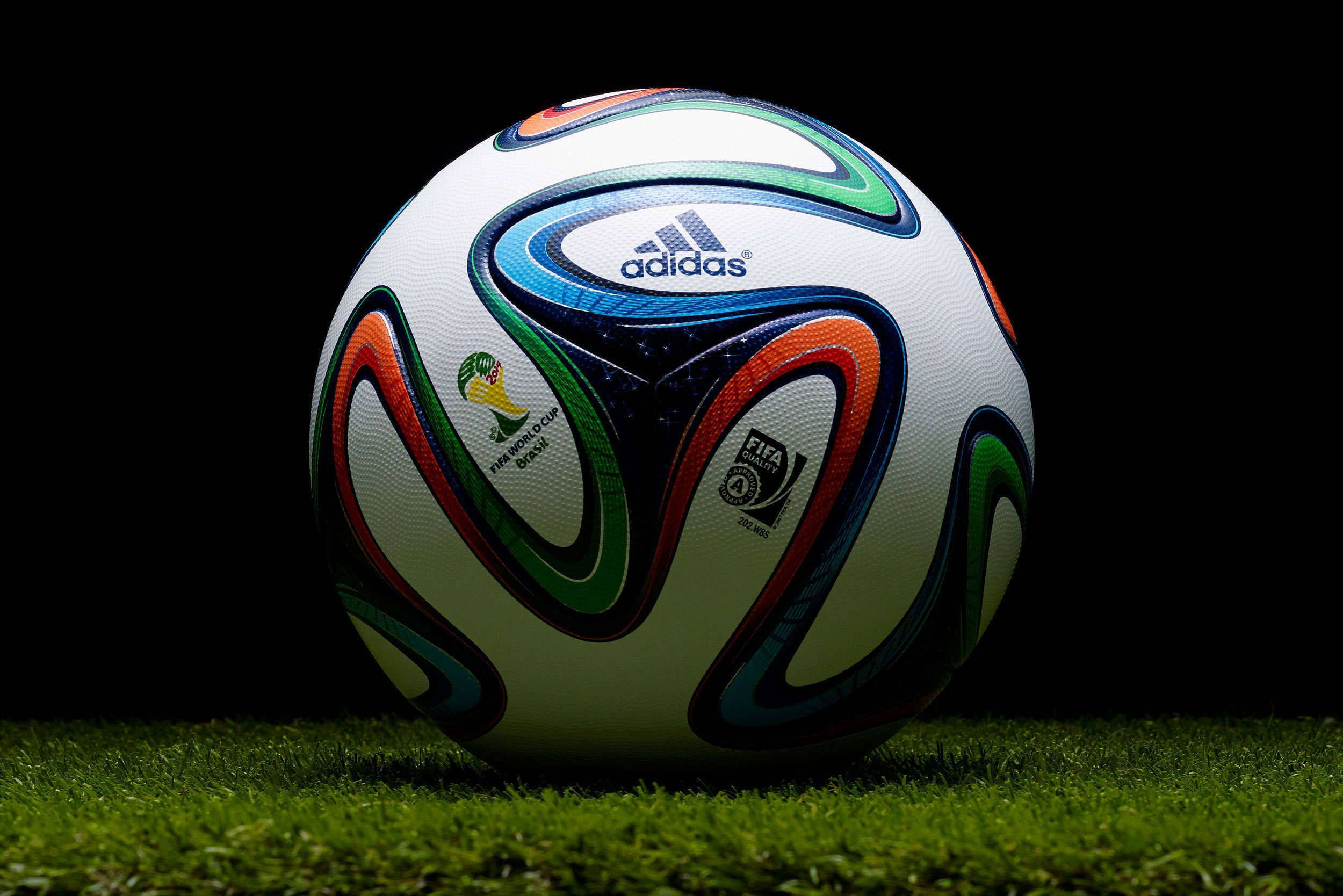 運動 桌布 壁紙 — 2014年FIFA世界盃巴西官方愛迪達足球的特寫，放置在充滿活力的綠色草地上，背景為黑色。