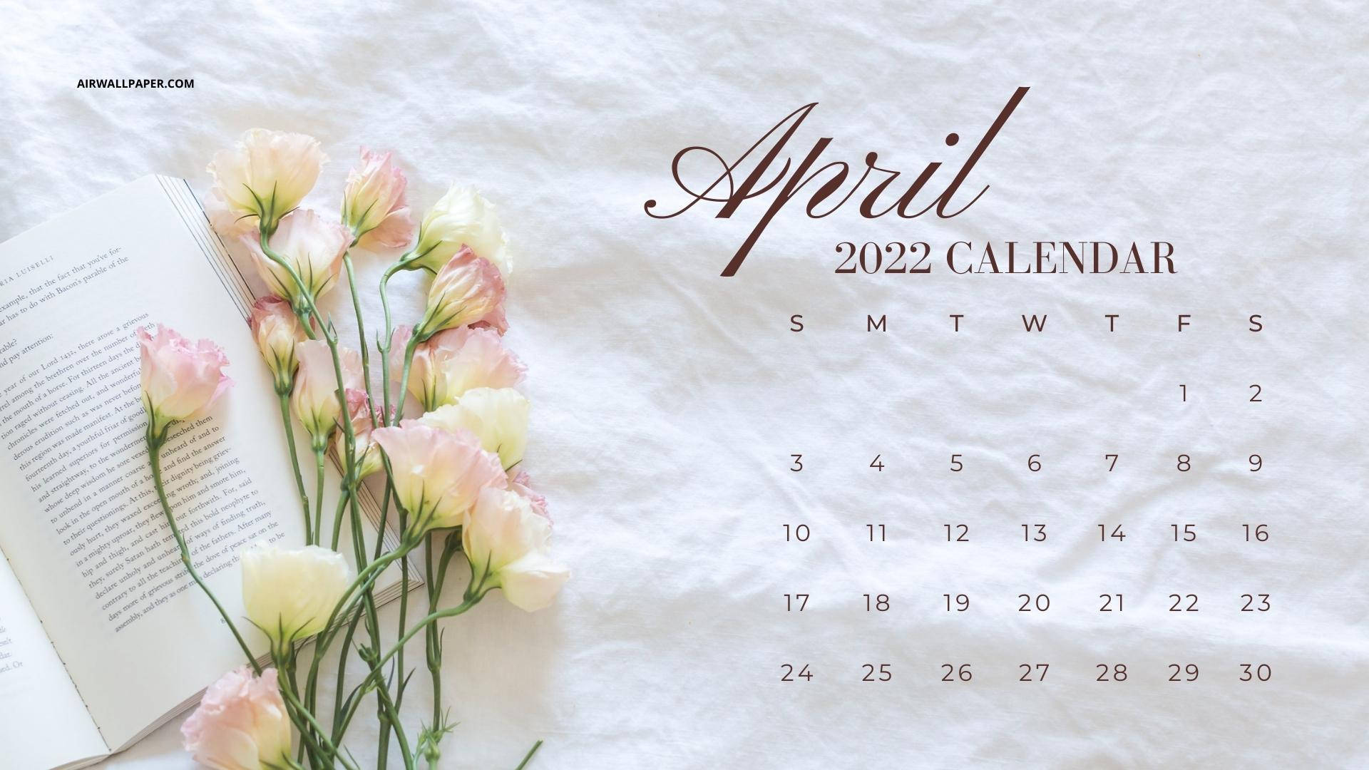 April 桌布 壁紙 — 2022年4月日曆優雅地展示在打開的書本和柔和的粉紅色花朵旁邊，放在有紋理的白色布料上。