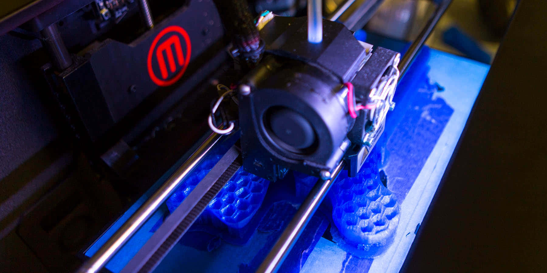3d Printer 桌布 壁紙 — 3D列印機在昏暗燈光下將藍色線材擠出到構建板上的特寫。
