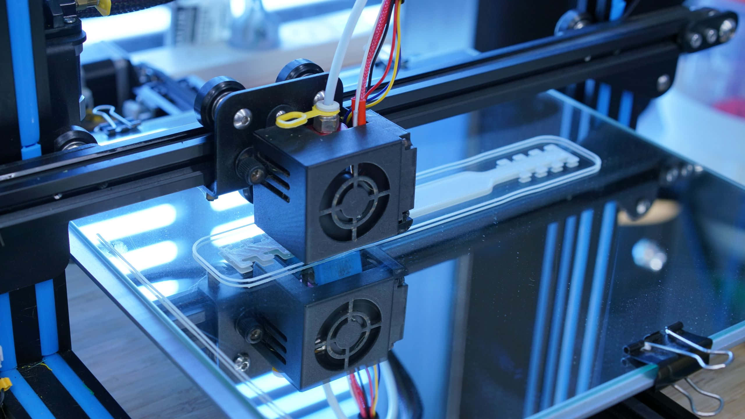 3d Printer 桌布 壁紙 — 3D列印機擠出器在藍光下將白色線材沉積到玻璃列印平台的近距離特寫。