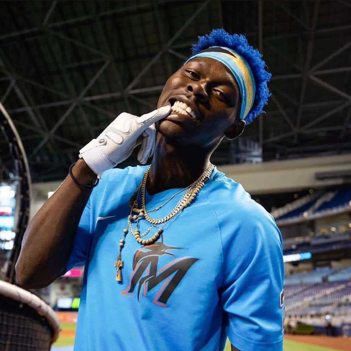  壁紙 — 一位藍色頭髮、身穿藍色球衣的棒球選手在體育館內微笑，同時用白色手套觸碰牙齒。