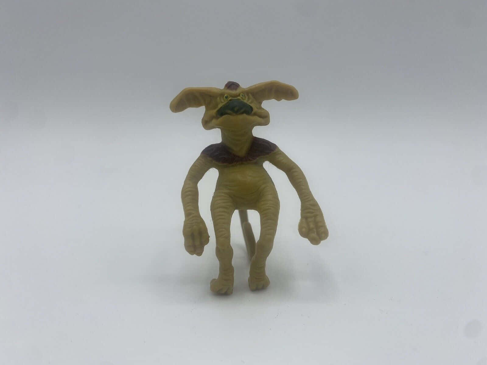 一個米色塑膠小魔怪玩具公仔站在白色表面上。 — 3D 壁紙
