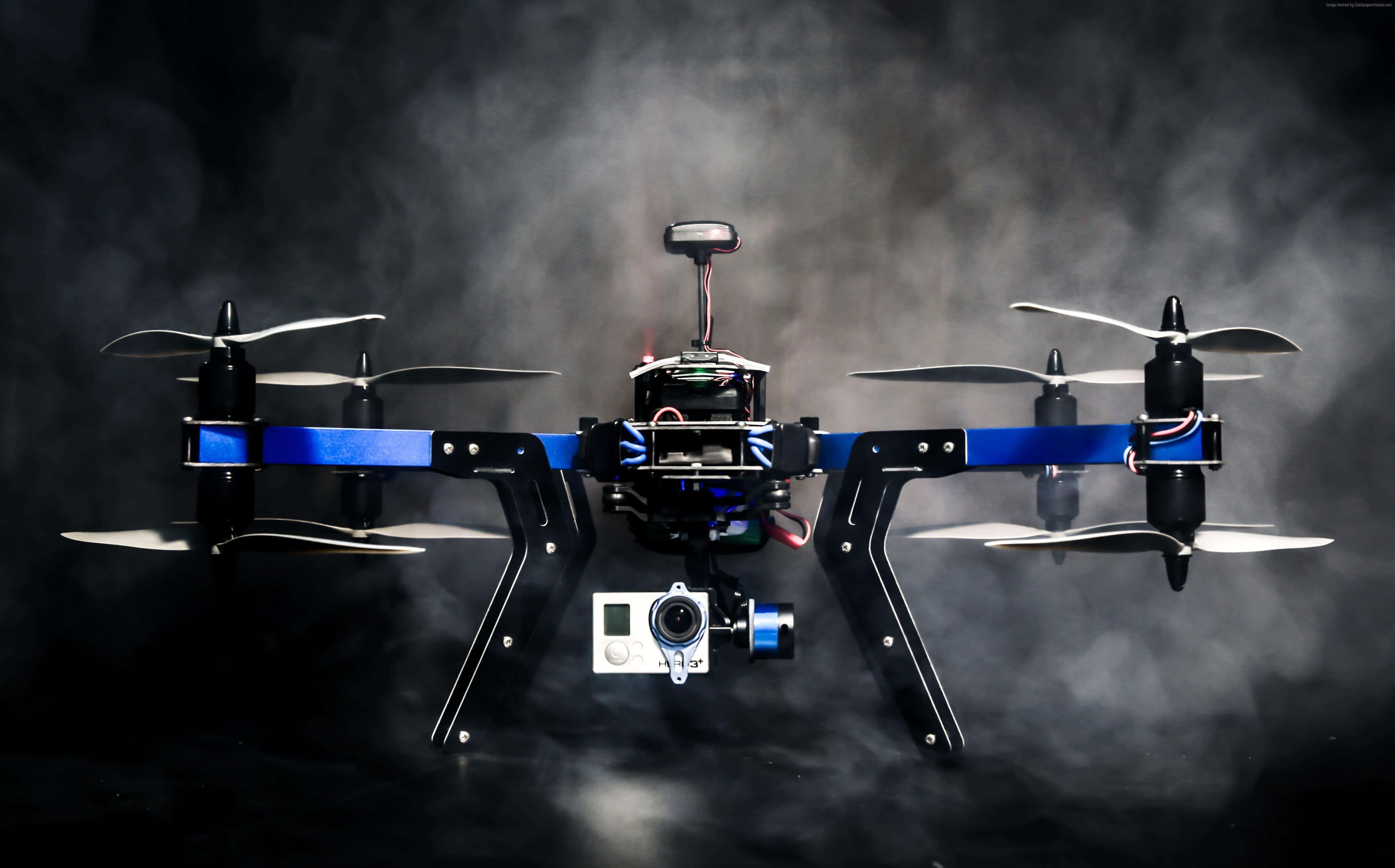 Drone Camera 桌布 壁紙 — 一台黑色和藍色的四軸無人機，帶有裸露的電線和安裝的攝影機，在煙霧瀰漫的黑暗中盤旋。