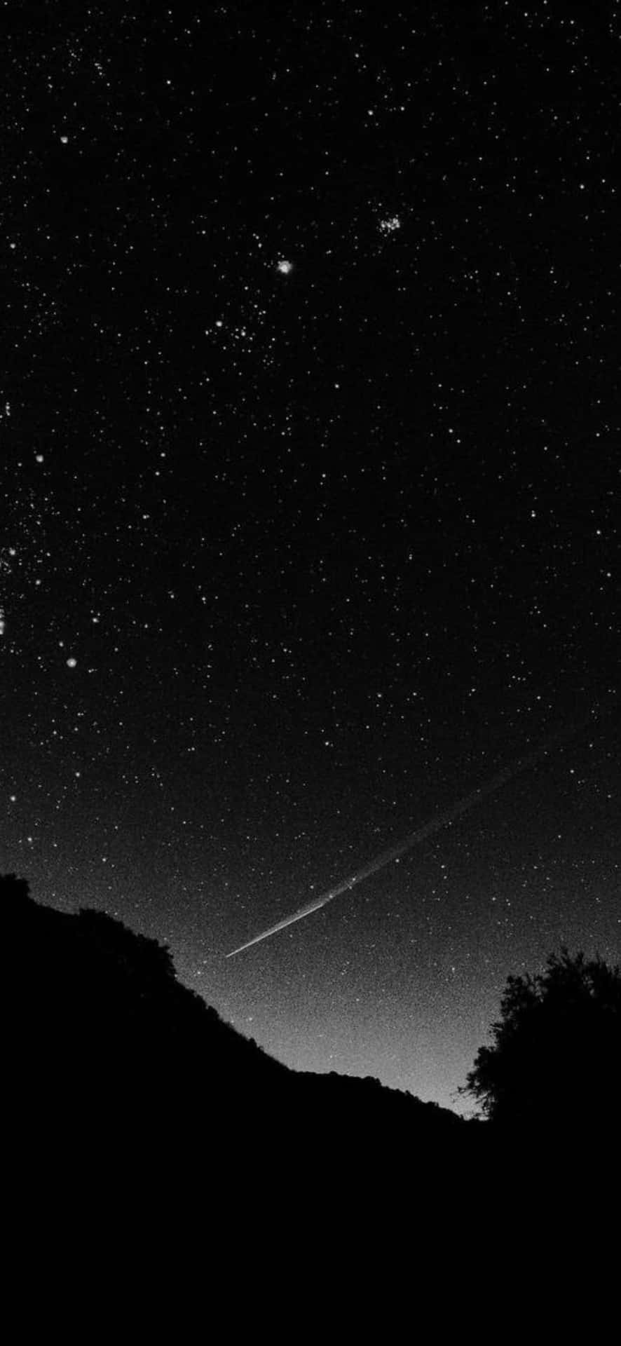  壁紙 — 黑白夜空，滿天繁星，一顆明亮的流星劃過黑暗剪影的山丘和樹木。