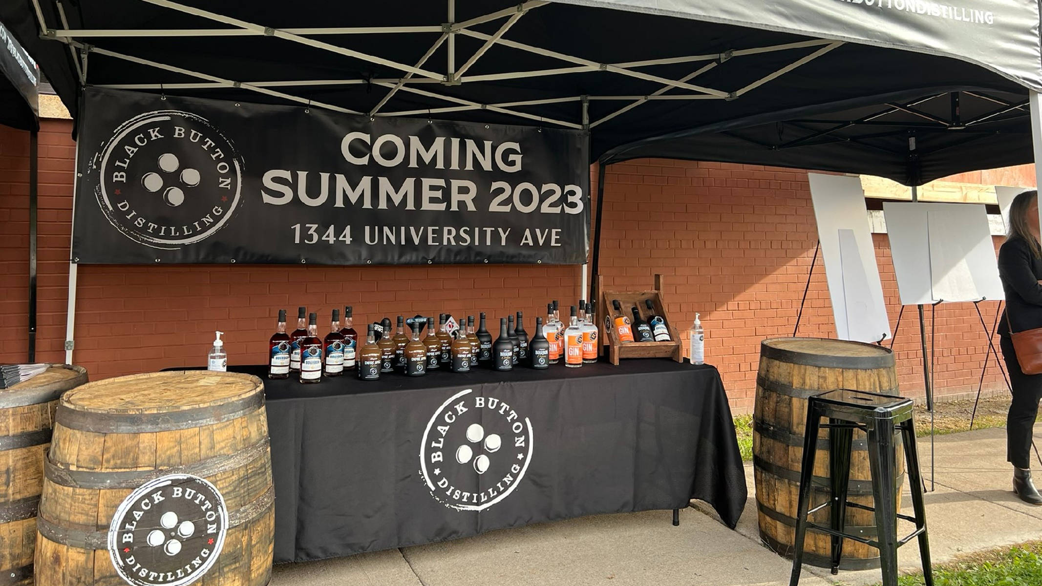 New 桌布 壁紙 — Black Button Distilling 攤位在帳篷下展示威士忌酒瓶，並有橫幅宣布2023年夏季開業。