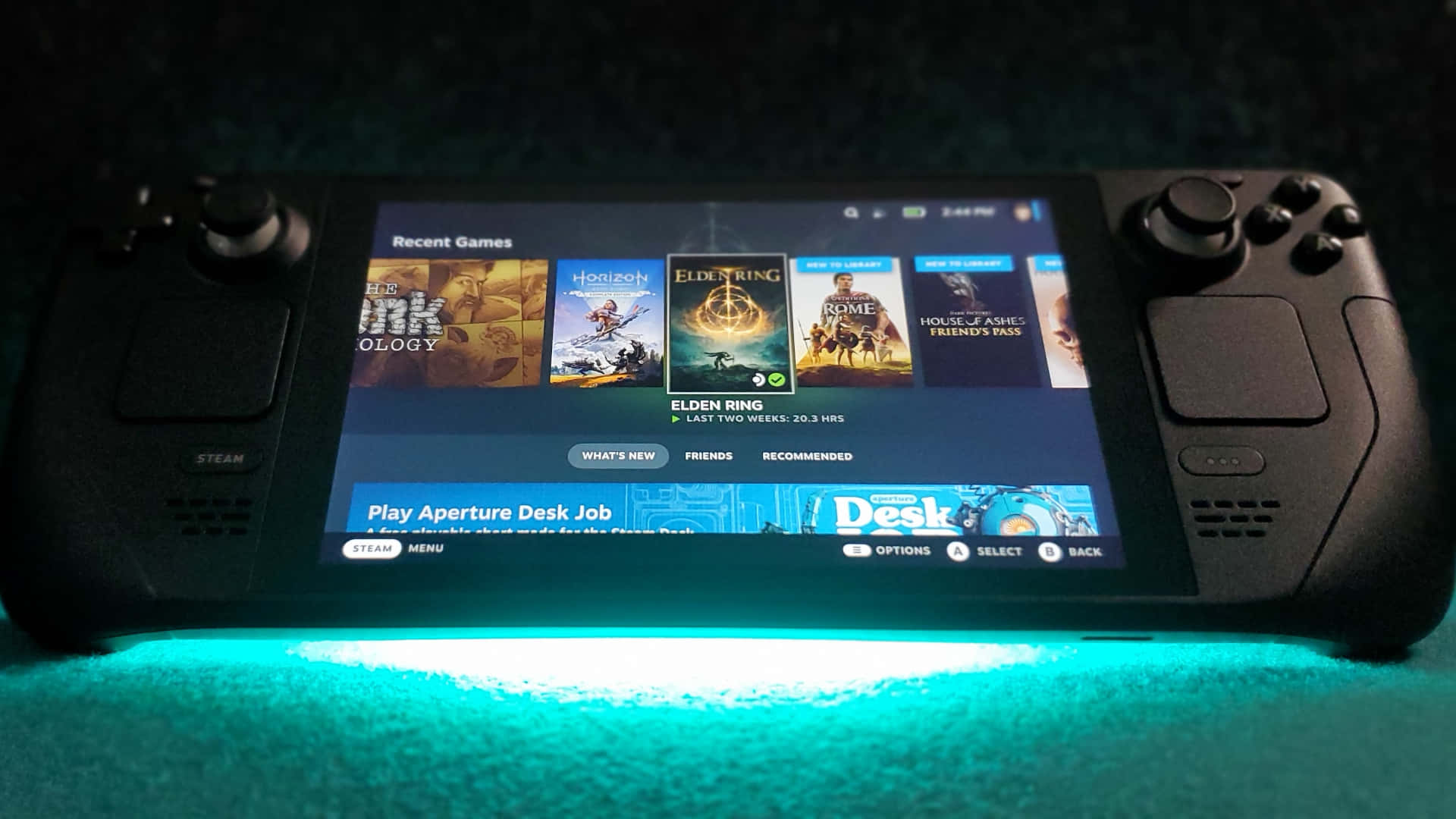  壁紙 — 一台黑色 Steam Deck 掌上遊戲機在螢幕上顯示《艾爾登法環》和《地平線》等近期遊戲，放置在青綠色發光表面上。
