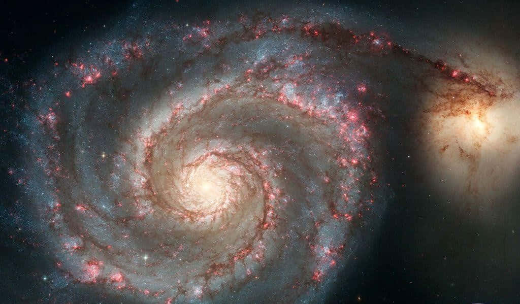 Spiral Galaxy 桌布 壁紙 — 一個令人嘆為觀止的螺旋星系，在繁星點點的宇宙虛空中旋轉著發光的粉紅色和藍色星雲。