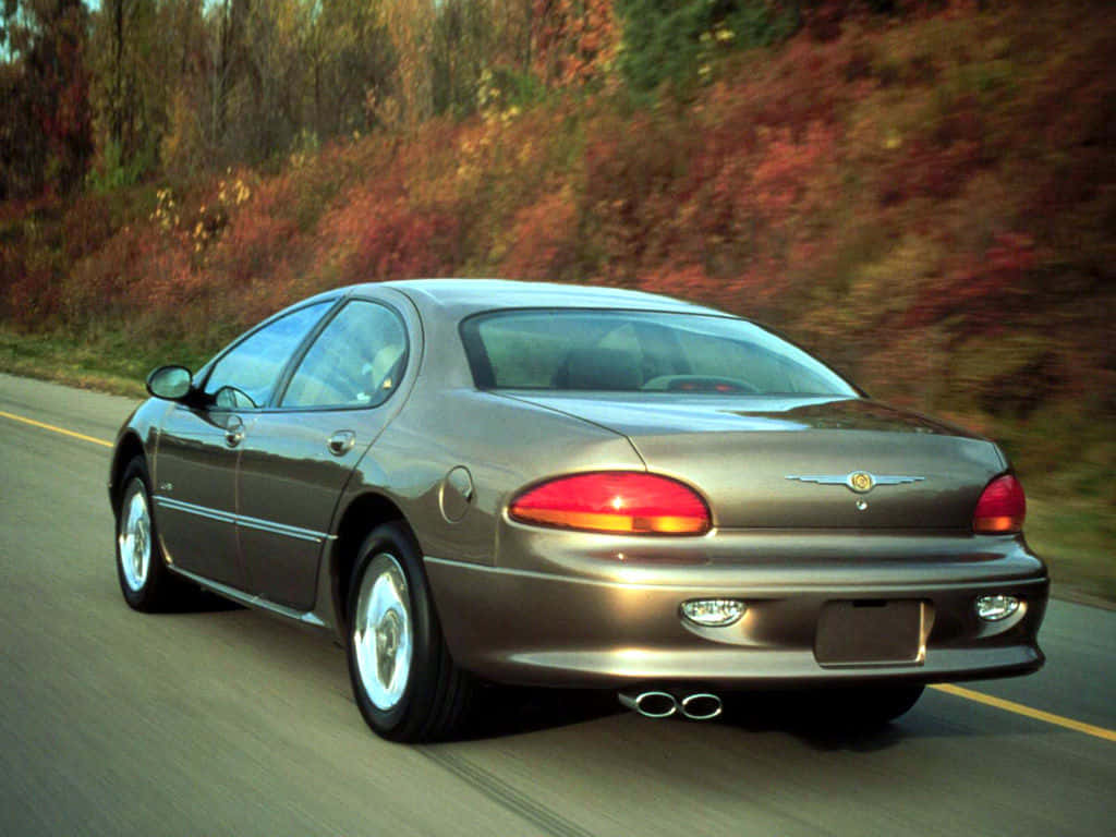 Chrysler Lhs 桌布 壁紙 — 一輛青銅色的克萊斯勒轎車沿著蜿蜒的道路行駛，兩旁是充滿活力的秋葉。
