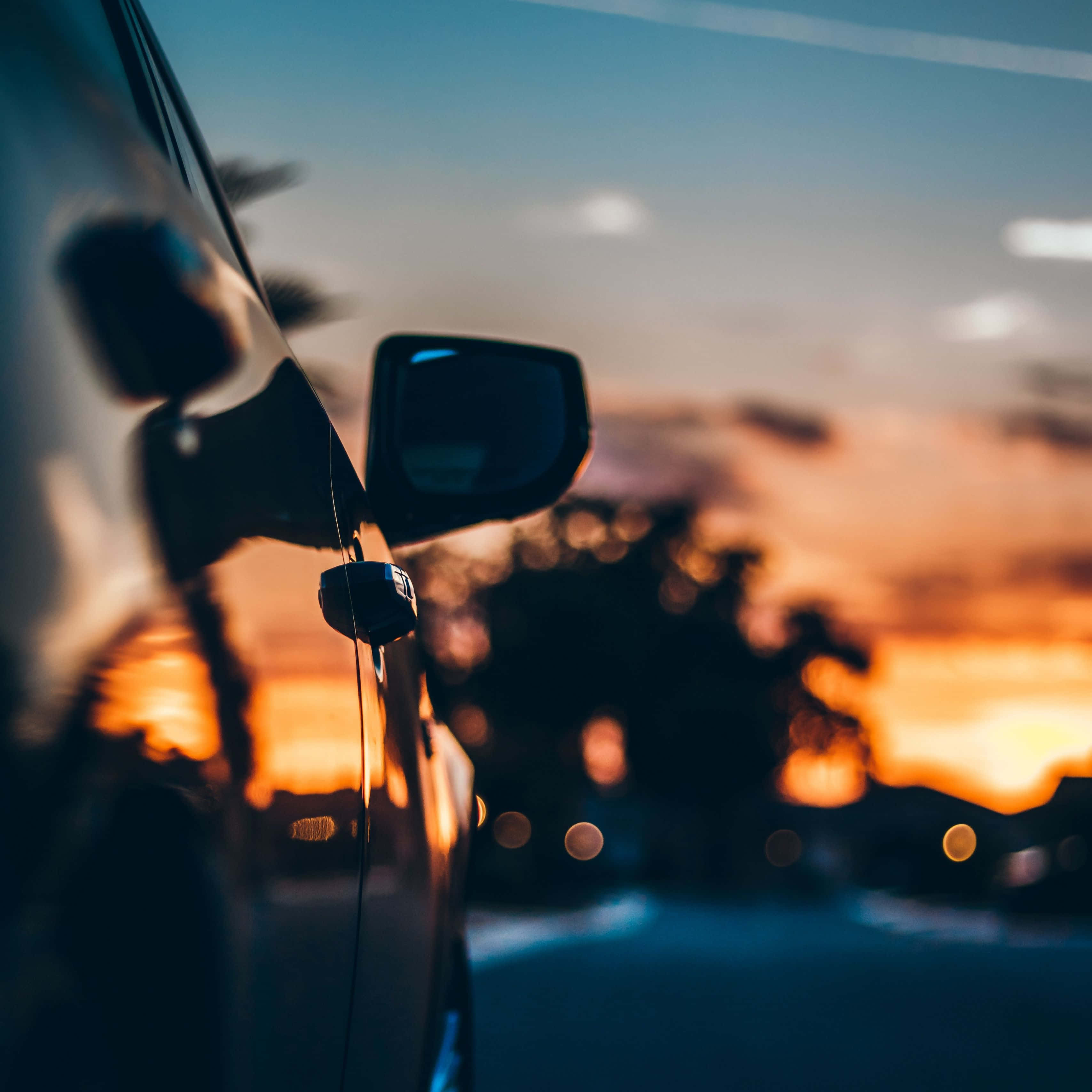 Sunset Drive 桌布 壁紙 — 汽車的側鏡反射出充滿活力的日落天空，帶有溫暖的橙色雲彩和模糊的城市燈光。