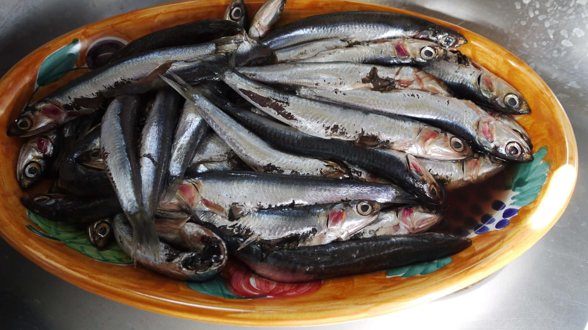  壁紙 — 一個陶瓷碗裝滿新鮮小魚，在不鏽鋼表面上閃閃發光。