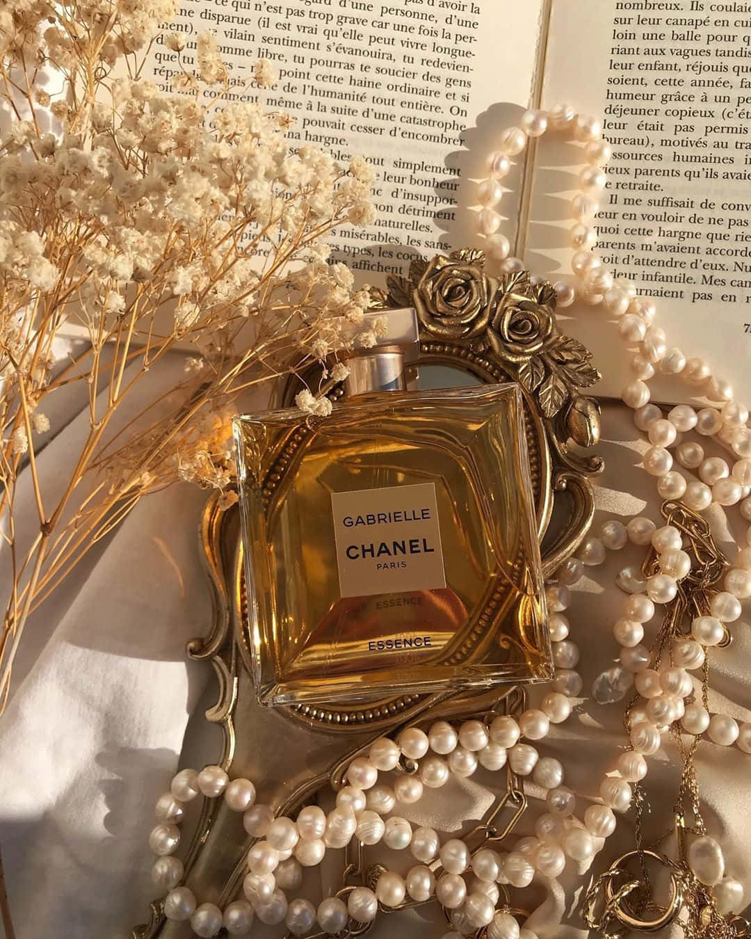 書本 桌布 壁紙 — Chanel Gabrielle Essence 香水瓶在金色光芒中閃耀，旁邊放有乾燥花、珍珠和一本打開的書。