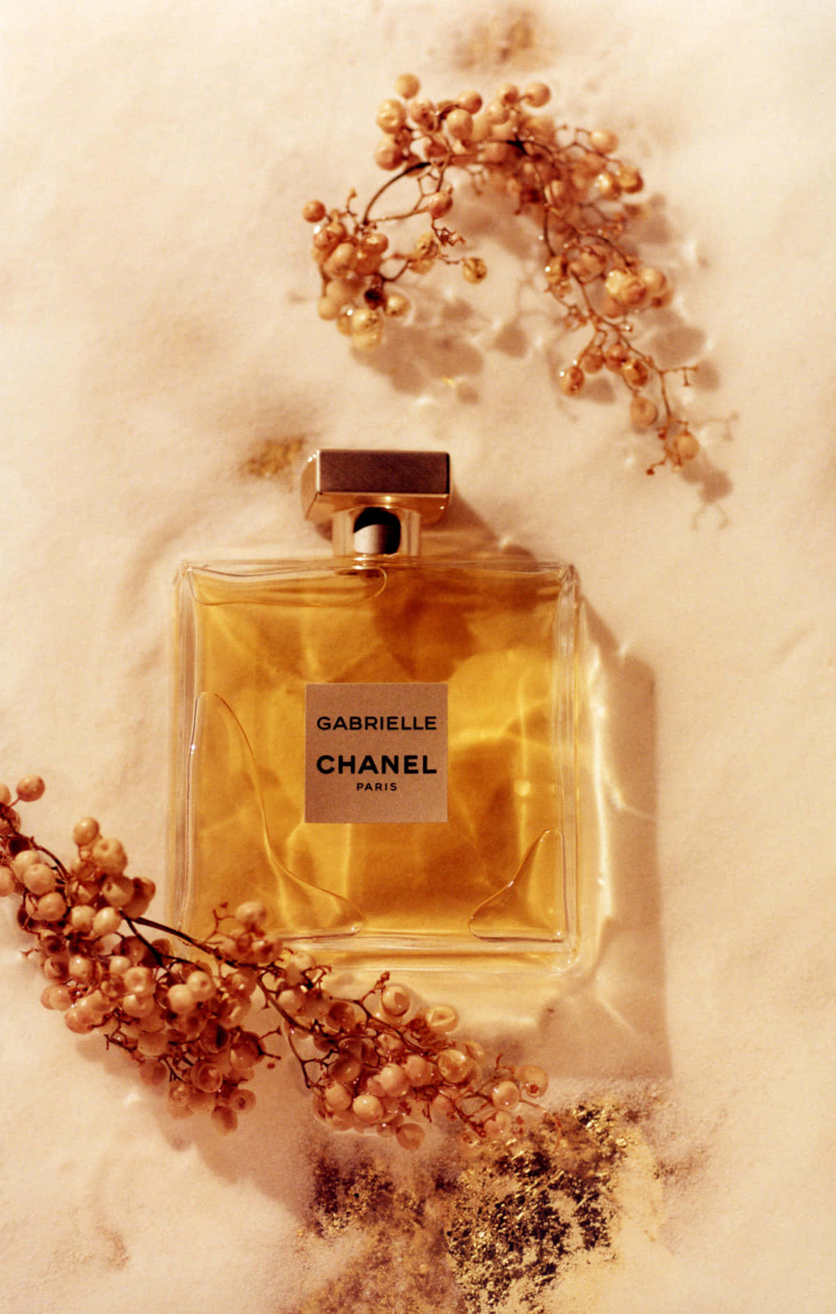Spring Perfume 桌布 壁紙 — Chanel Gabrielle 香水瓶放在淺水中，周圍是乾燥的金色漿果，置於有紋理的米色表面上。