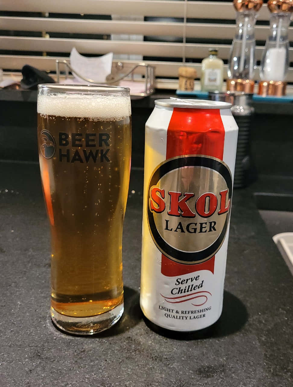  壁紙 — 一罐冰涼的Skol Lager啤酒放在室內燈光下的深色檯面上，旁邊有一個泡沫啤酒杯。