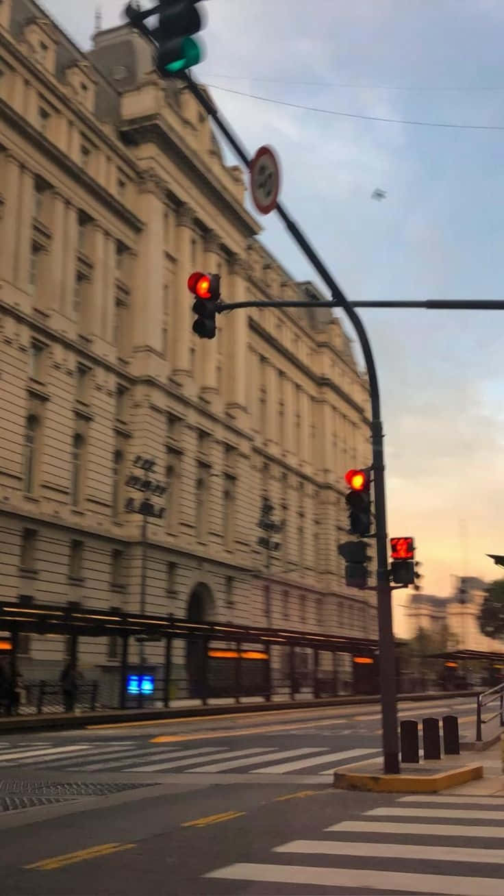  壁紙 — 黃昏時分的城市街道，紅色交通燈在歷史建築外牆和柔和橙色天空的映襯下閃耀。
