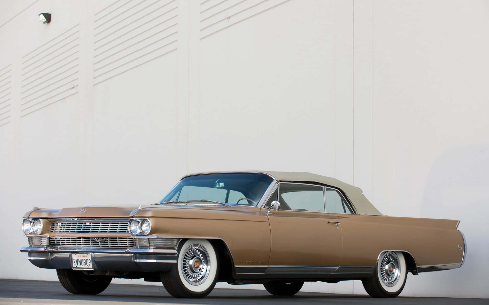 Cadillac Eldorado 桌布 壁紙 — 一輛經典的棕色敞篷車配備白色側壁輪胎，在明亮的日光下停放在極簡白色牆壁前。