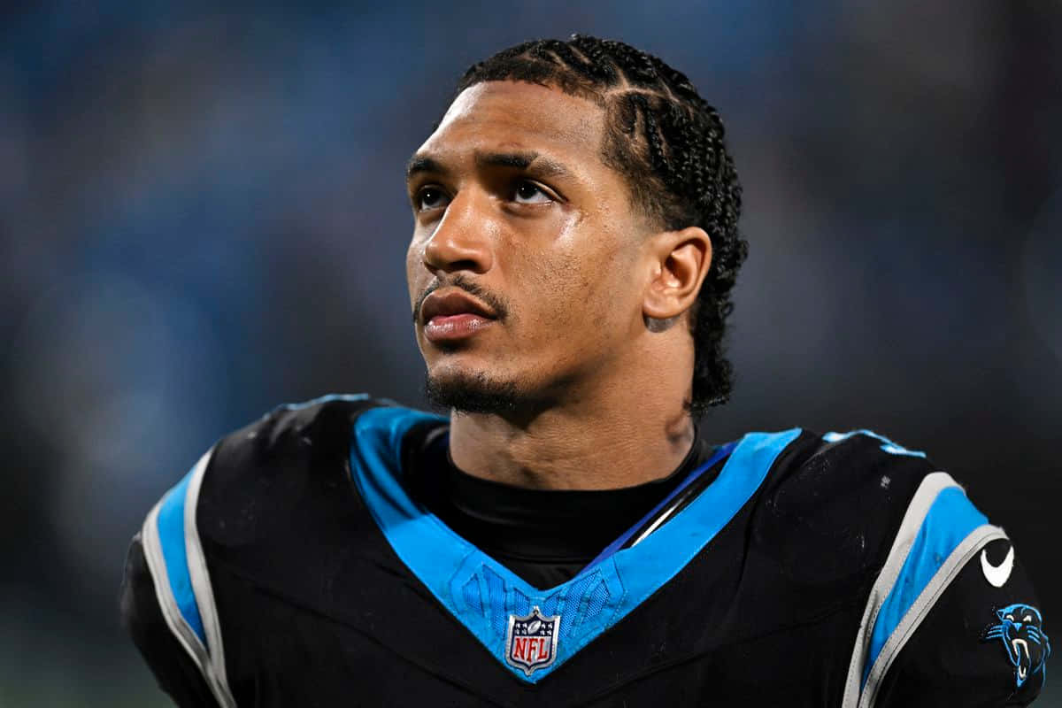 壁紙 — 球場燈光下，一位專注的NFL美式足球員身穿黑藍色卡羅萊納黑豹隊球衣的特寫。