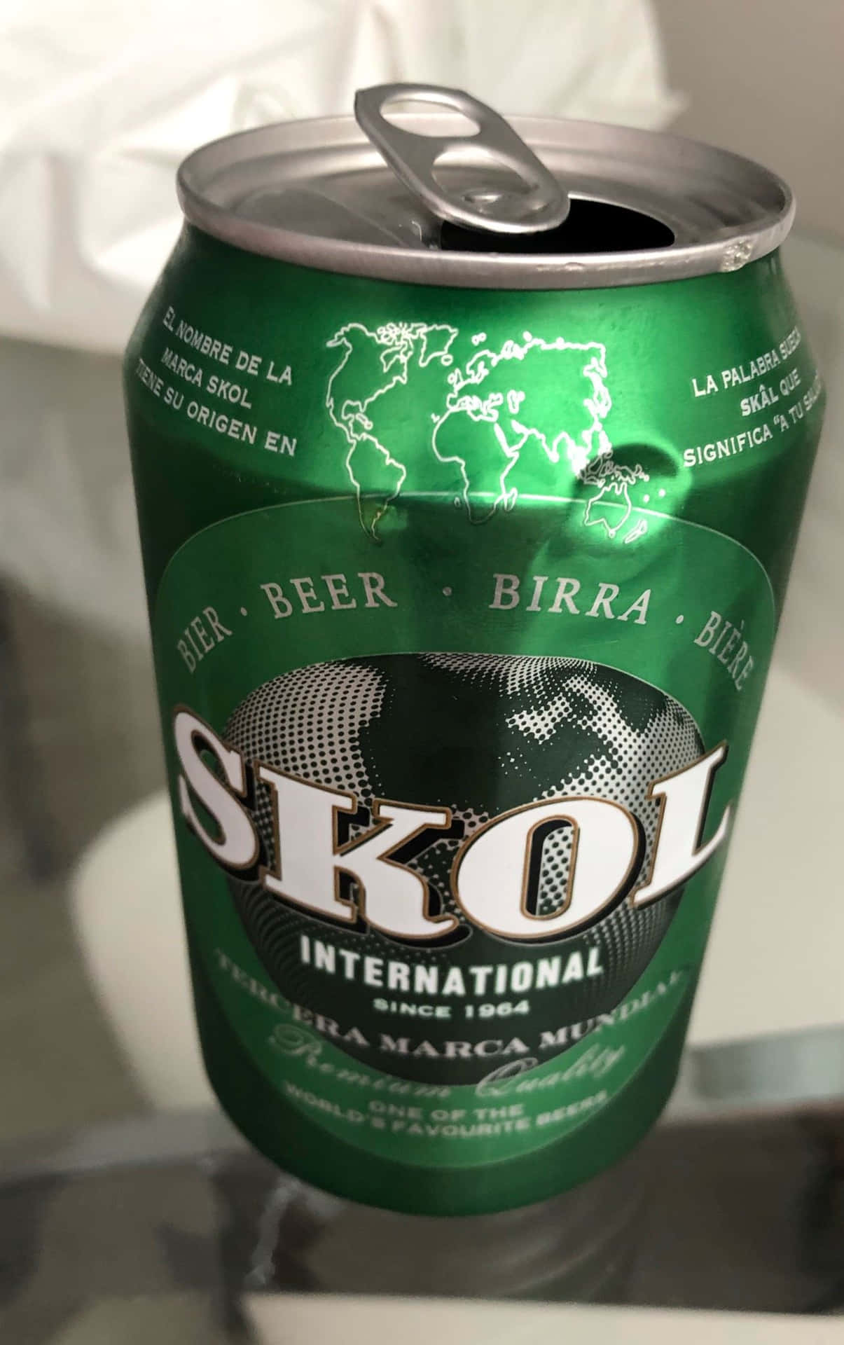  壁紙 — 一個綠色Skol啤酒罐的特寫，帶有彈出的拉環和地球標誌，位於反光表面上。