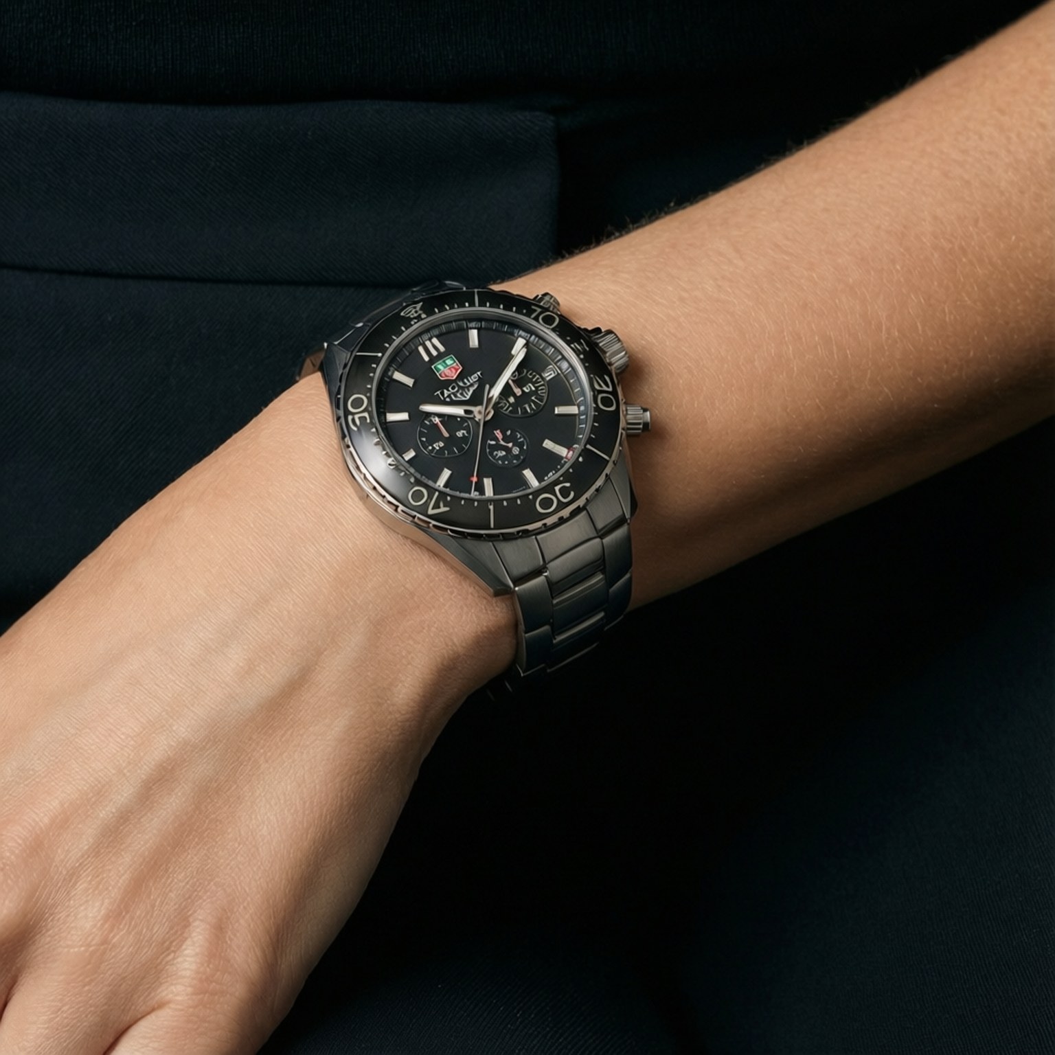 Tag Heuer Elegance 壁紙 — 近距離拍攝一只時尚黑色Tag Heuer手錶戴在人的手腕上，背景為深色布料。