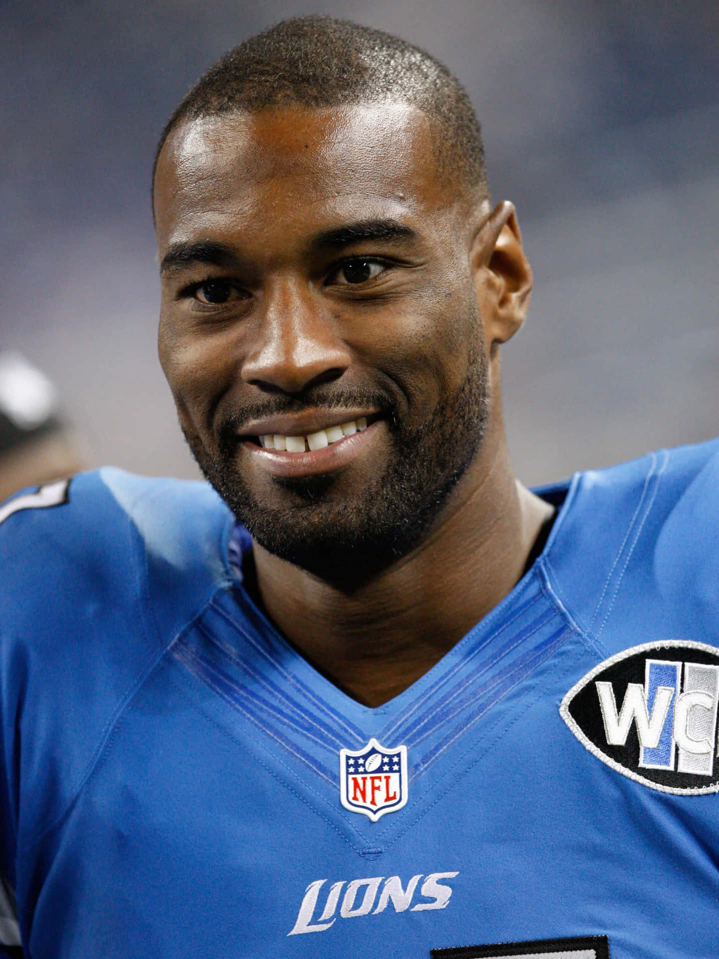  壁紙 — 一名微笑的NFL足球員身穿藍色獅子隊球衣，帶有NFL和世界盃補丁的特寫。