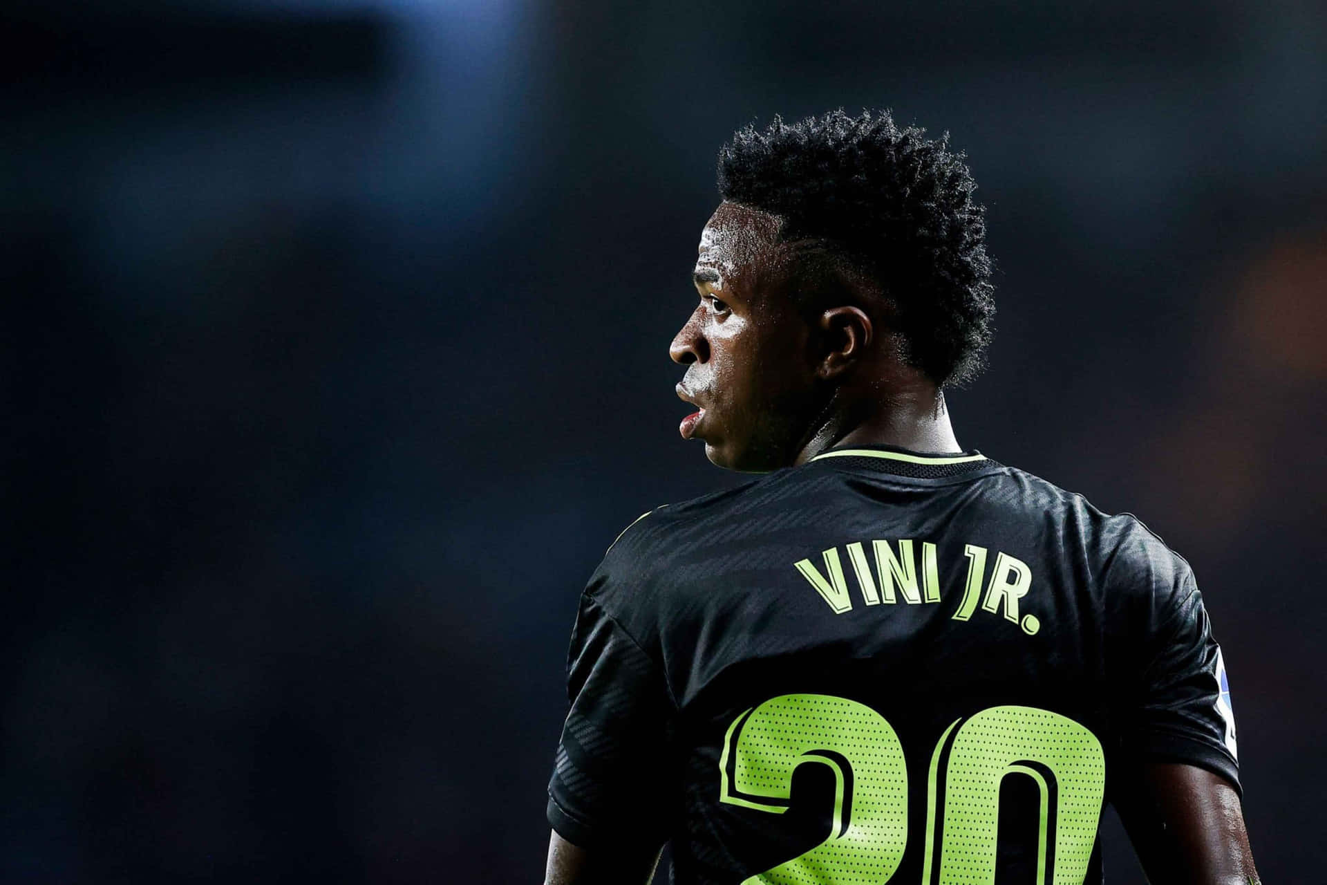  壁紙 — 一名足球員身穿黑色球衣，上面有螢光綠色「VINI JR.」和20號，在球場燈光下以側面特寫拍攝。