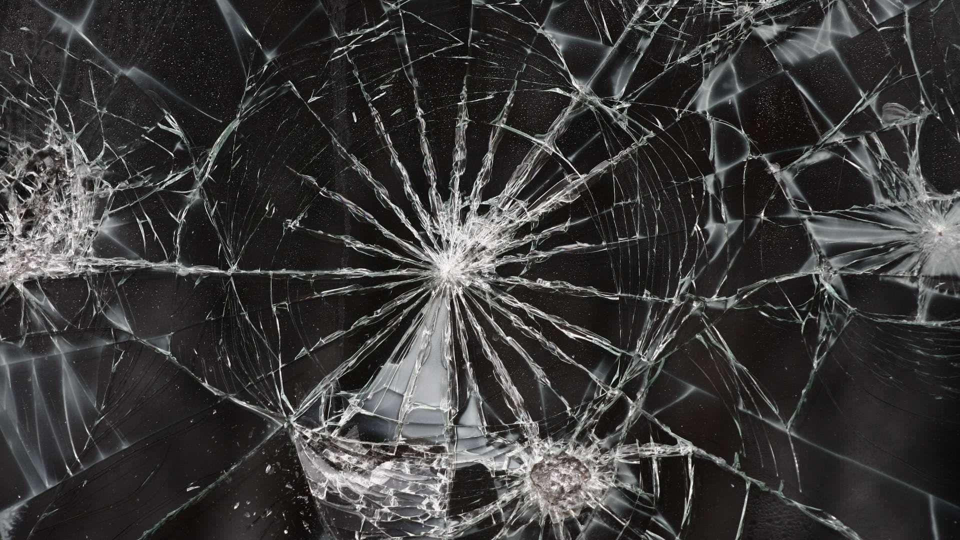  壁紙 — 特寫鏡頭，顯示在深色背景上，從撞擊點向外輻射的複雜裂紋的破碎玻璃。