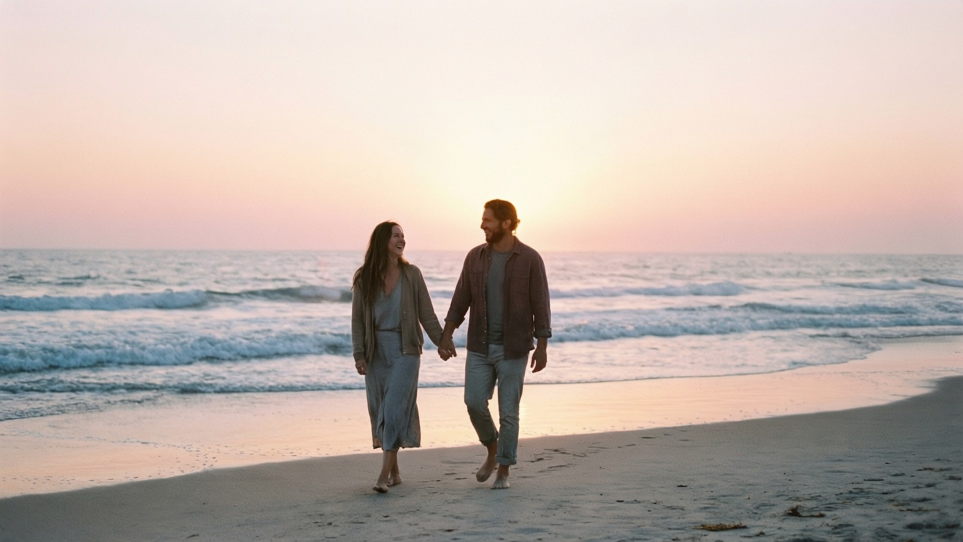 Beach Sunrise Walk 壁紙 — 一對情侶手牽手沿著沙灘漫步，夕陽西下，身後有溫柔的海浪翻滾。