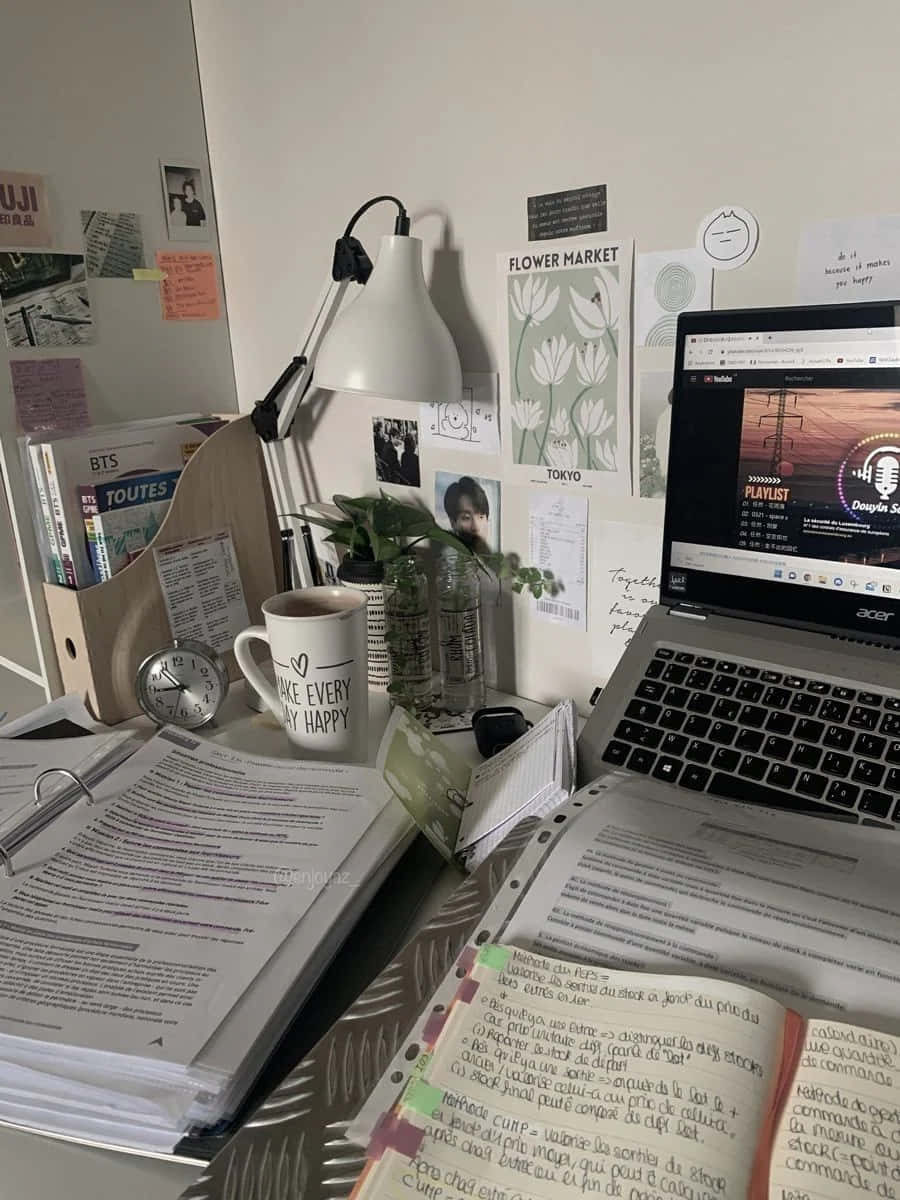  壁紙 — 一個舒適的書桌，上面有打開的筆記本、顯示音樂播放清單的筆記型電腦、一盞白色檯燈，以及釘在牆上的勵志便條。