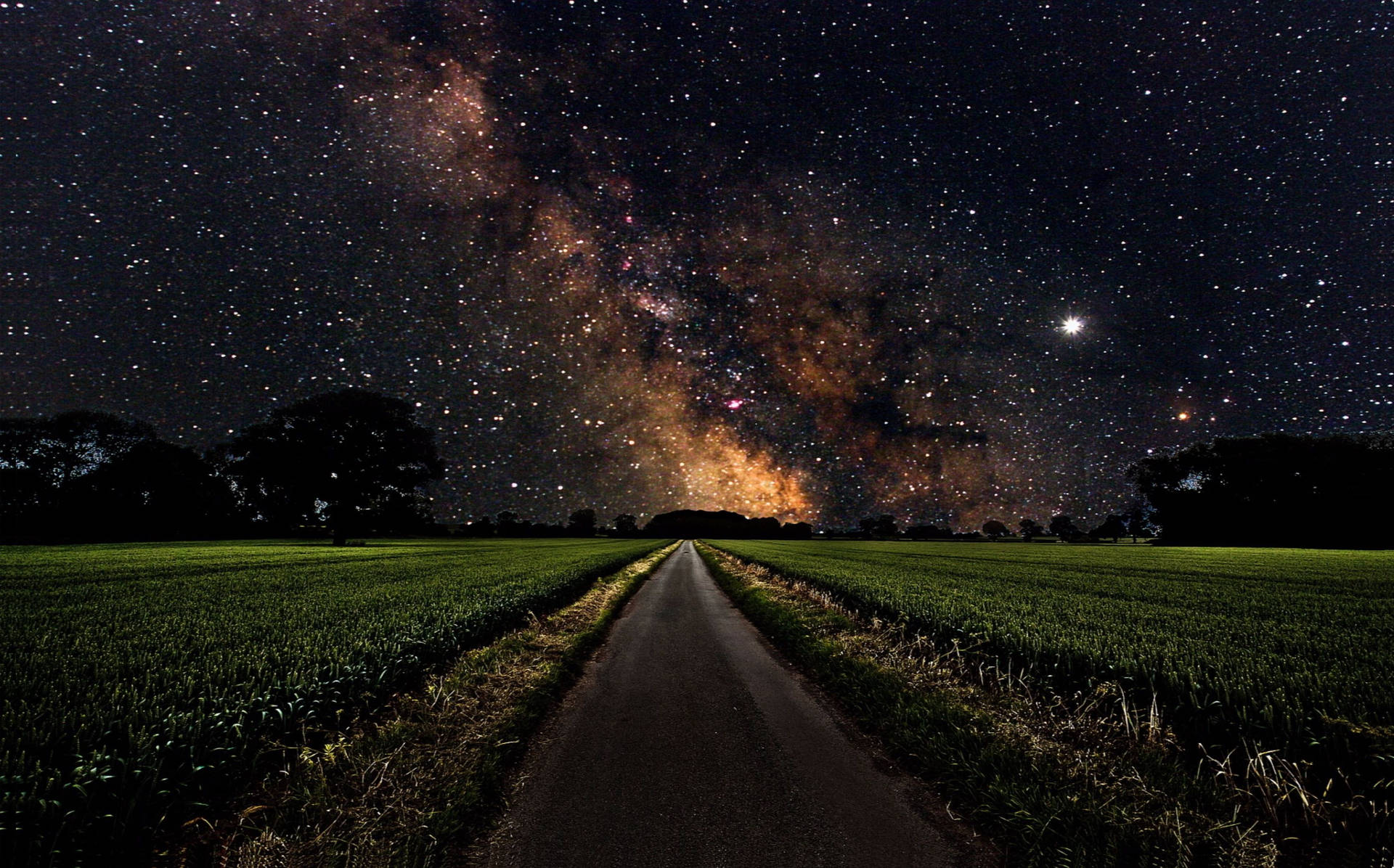 一條道路穿過田野，在星空下，銀河系清晰可見。 — 4K 太空 壁紙