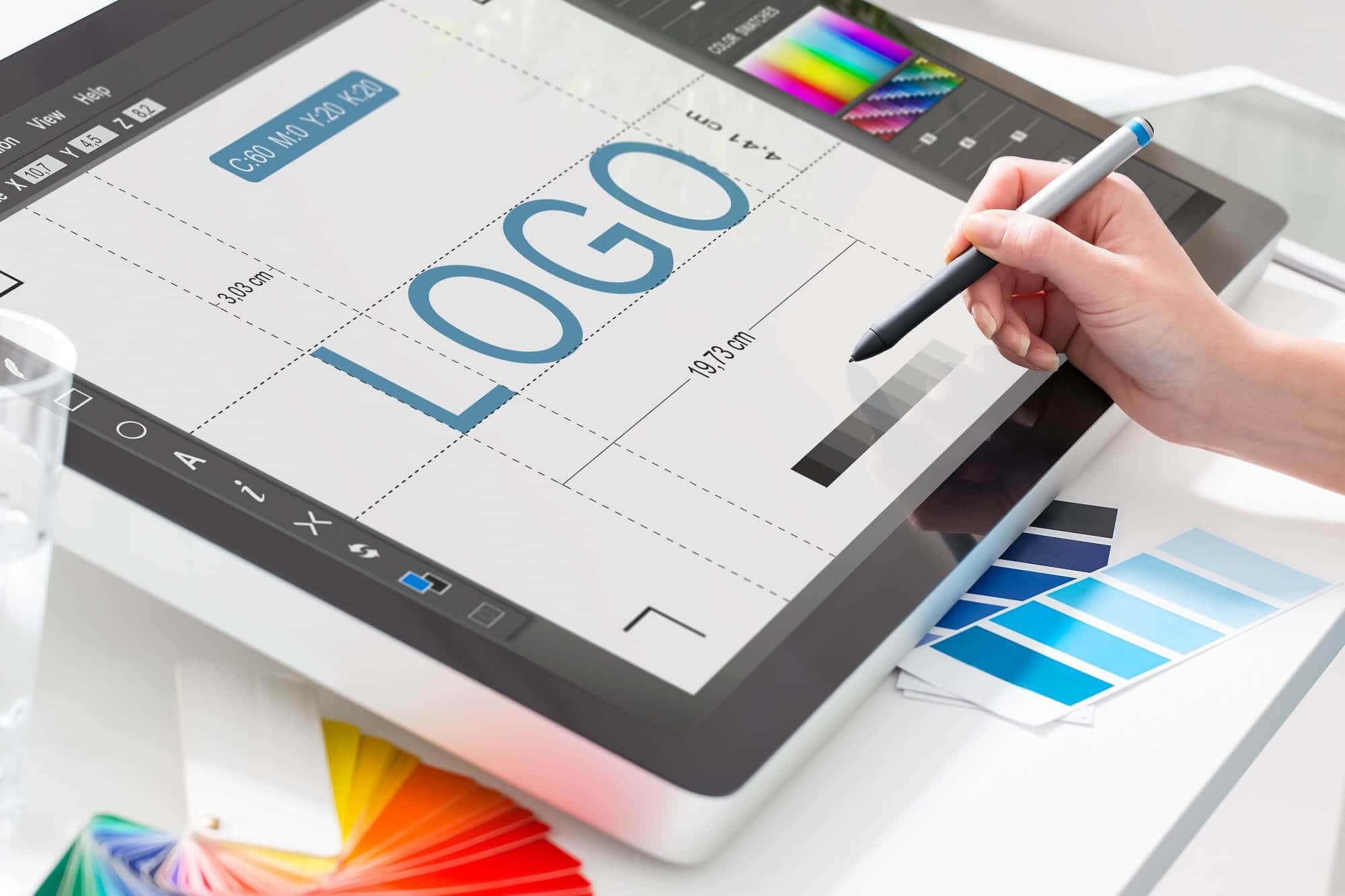 graphic design 桌布 壁紙 — 設計師的手用觸控筆在數位平板上創建一個藍色標誌，周圍環繞著色板。