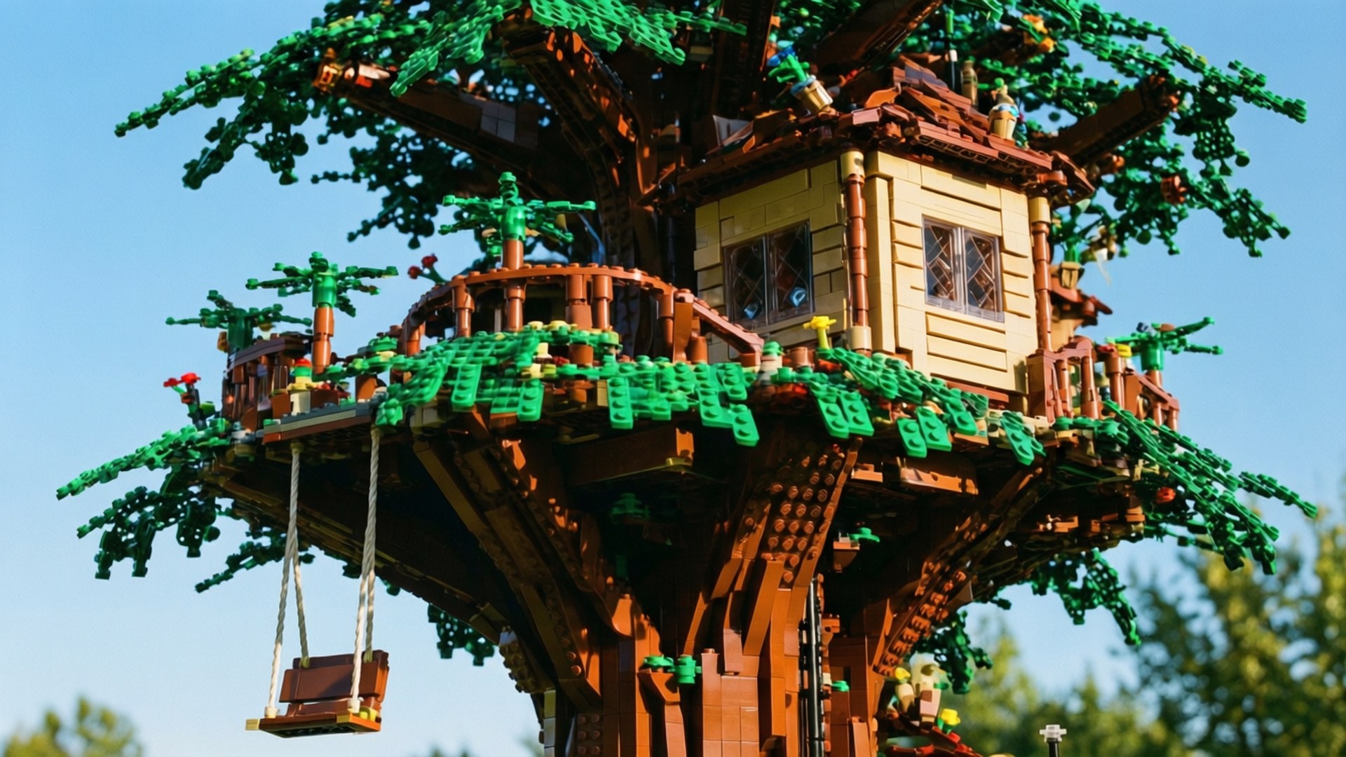Lego Treehouse Paradise 壁紙 — 一個詳細的LEGO樹屋，有綠色樹葉、棕色橫樑和一個鞦韆，襯托著清澈的藍天。