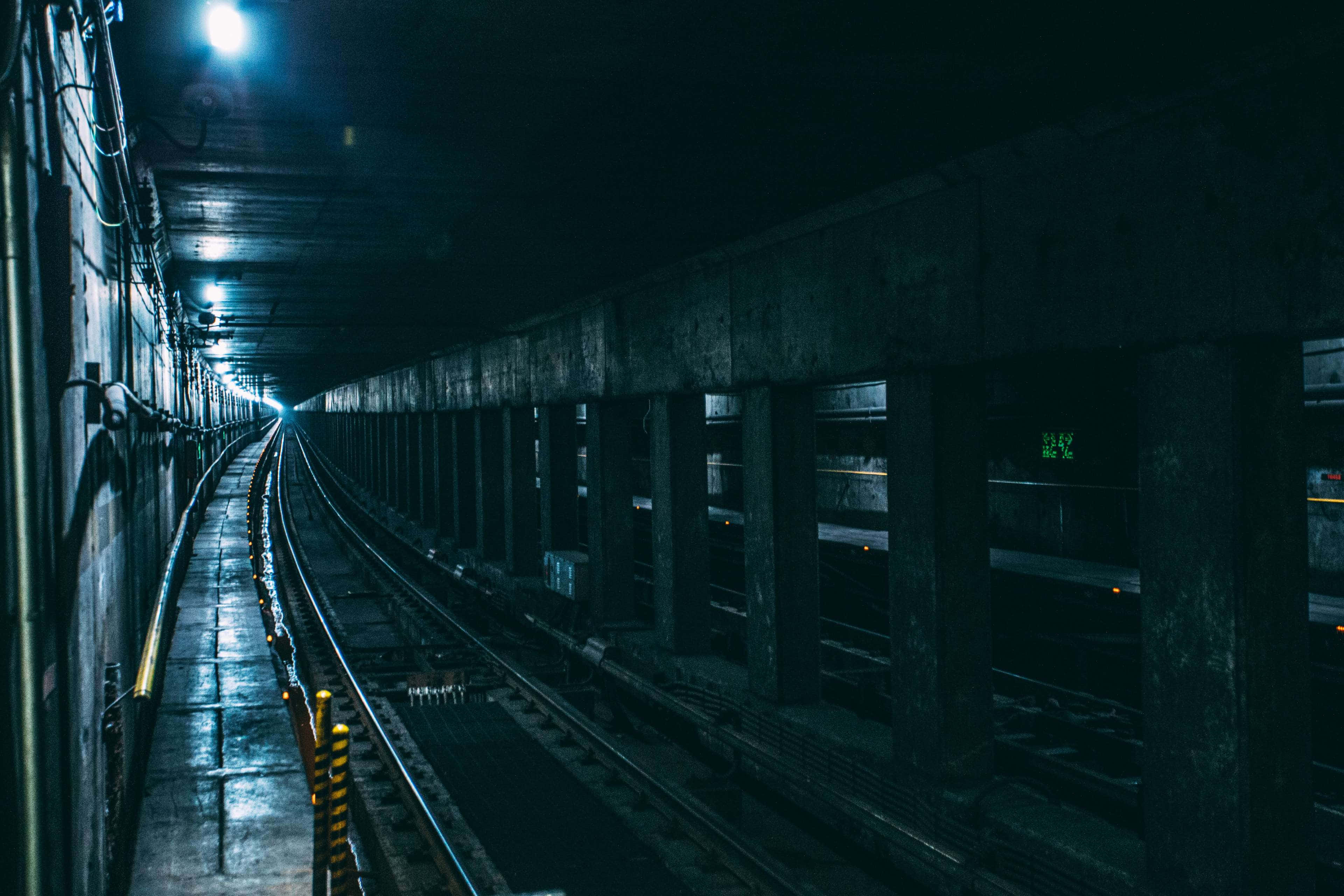 Dark Underground 桌布 壁紙 — 一條燈光昏暗的地鐵隧道，潮濕的軌道在頭頂單一燈光下延伸至遠方。