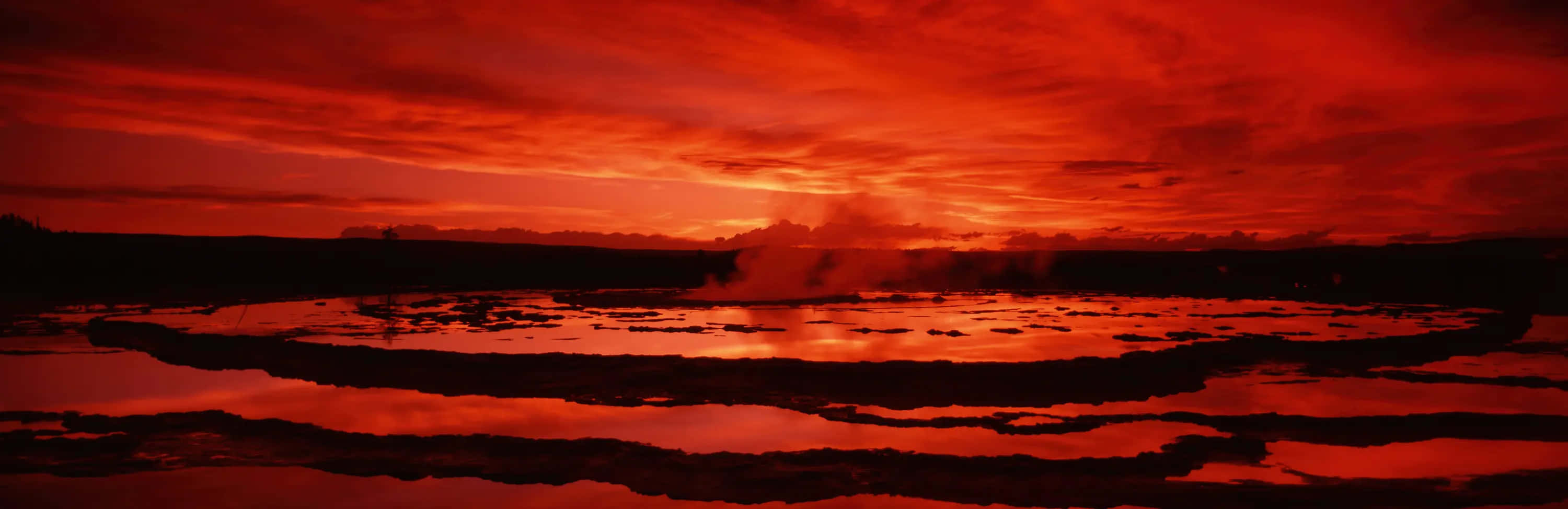  壁紙 — 火紅的夕陽在冒著蒸汽的地熱池上投射出戲劇性的倒影，伴隨著黑暗的輪廓地貌。