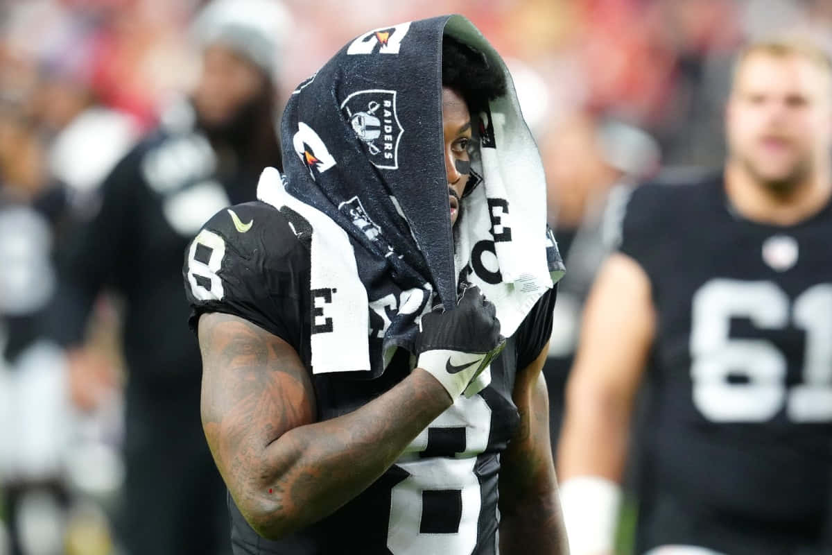  壁紙 — 一名身穿黑白 Raiders 球衣的足球員在比賽期間用球隊毛巾擦臉。