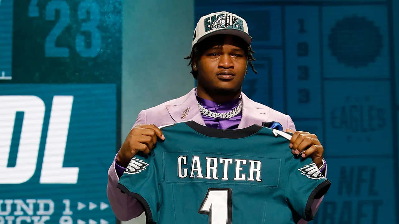  壁紙 — 一名足球員在選秀活動中自豪地舉起他的新Eagles球衣，身穿粉紅色西裝和帽子。