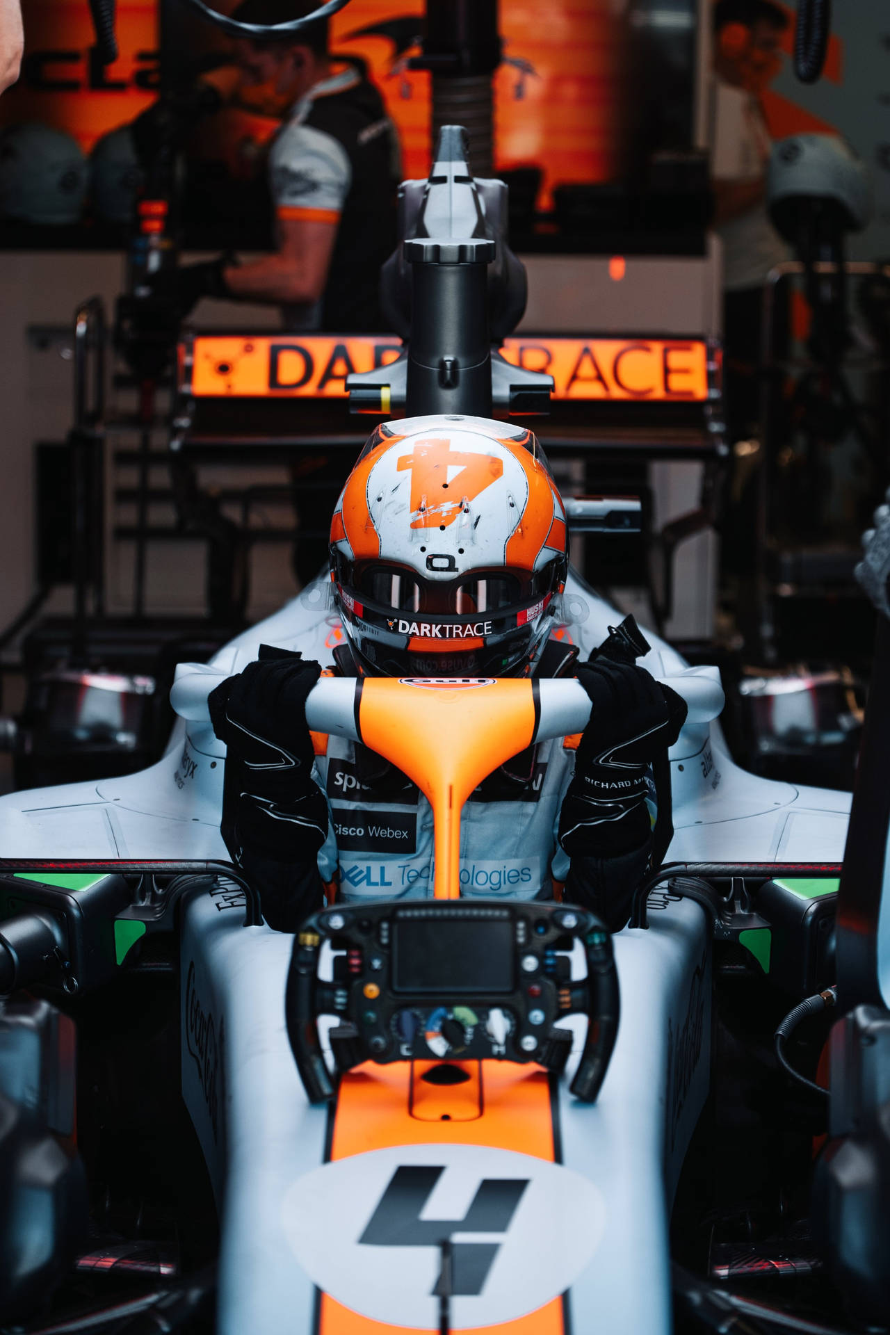 戴著橙色和白色頭盔的F1車手在賽車內，帶有贊助商標誌。 — F1 iPhone 壁紙 壁紙