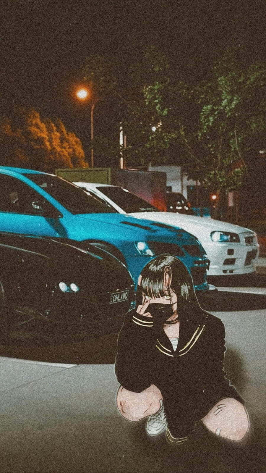  壁紙 — 一個穿著水手服的女孩在夜晚的街道上，蹲在街燈下停泊的汽車旁邊。