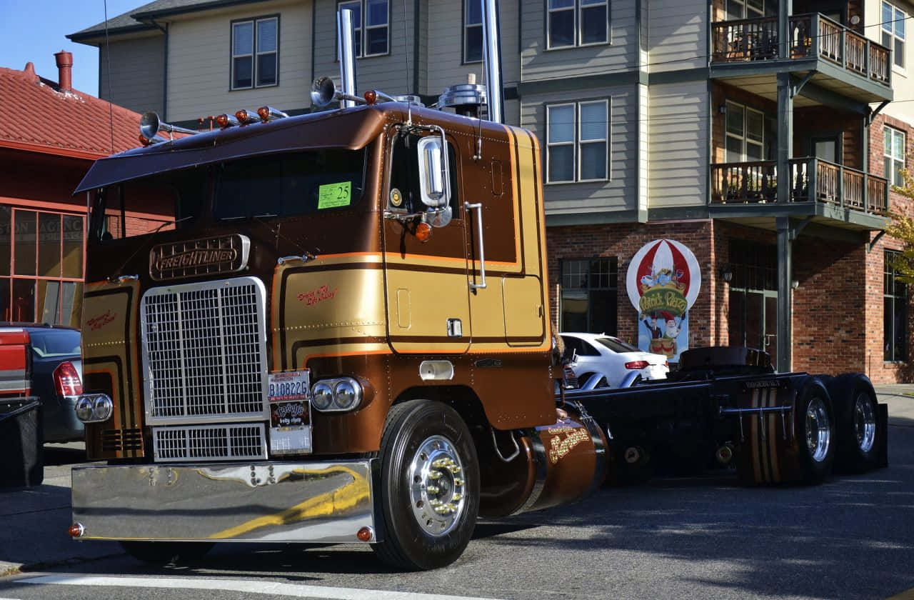 Kenworth T604 桌布 壁紙 — 一輛閃亮的棕色和金色經典半掛卡車停在一棟帶陽台的多層建築前。