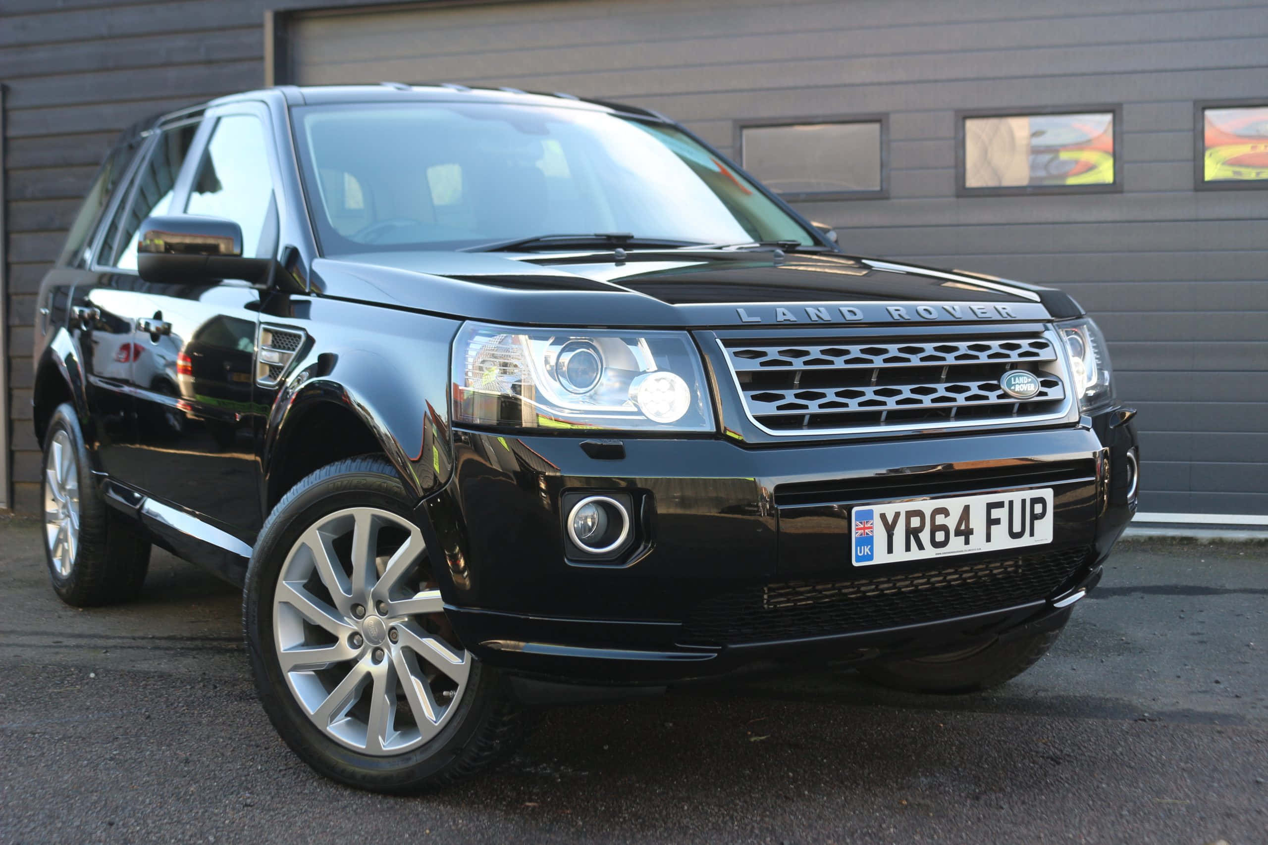 Land Rover Freelander 桌布 壁紙 — 一輛亮黑色Land Rover Freelander 2停放在現代灰色車庫前，配備反光鍍鉻輪圈。