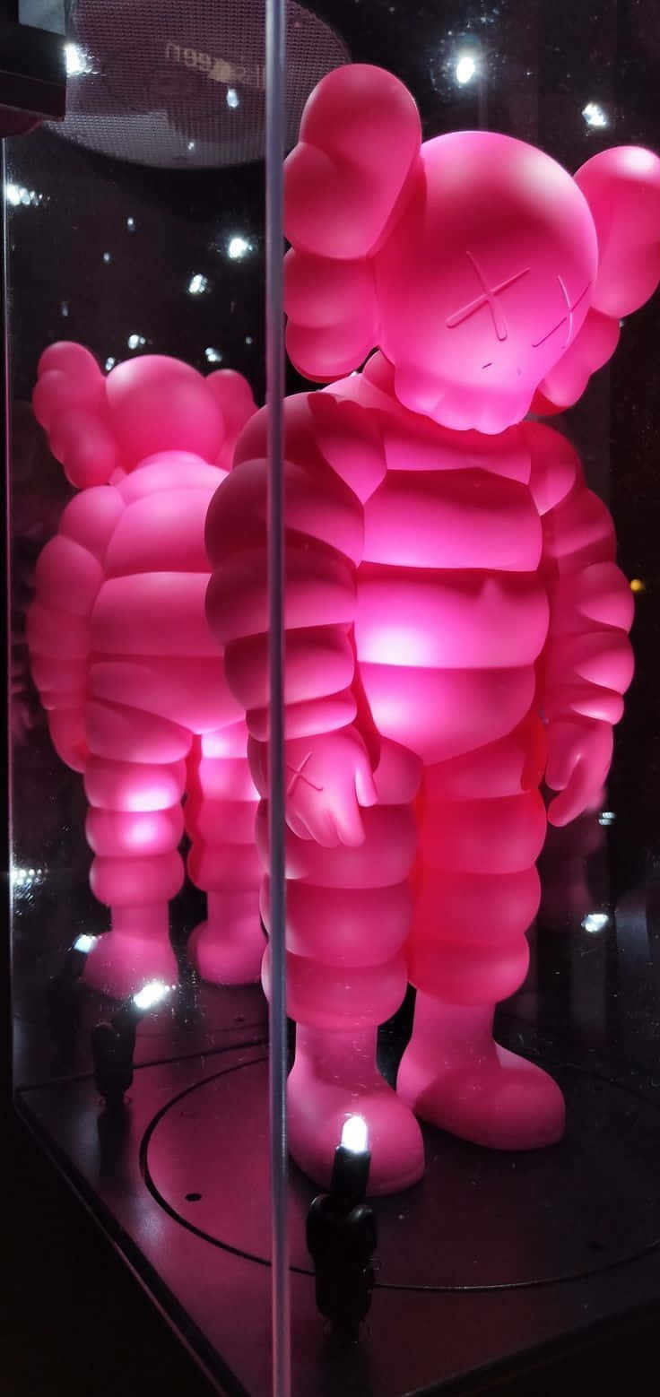 壁紙 — 一個發光的粉紅色KAWS雕塑在玻璃展示櫃內被照亮，其倒影清晰可見。