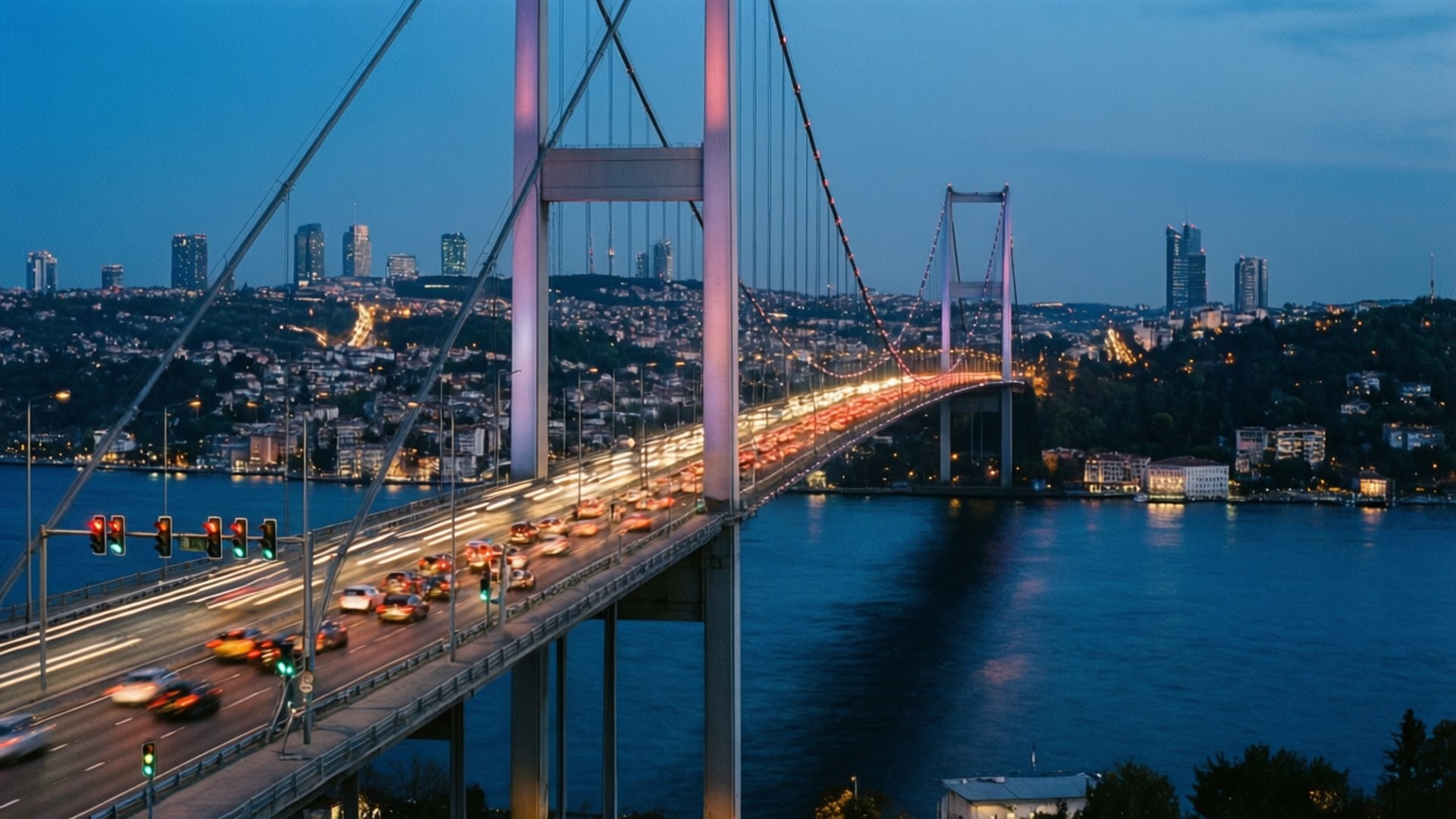 Bosphorus Bridge at Dusk 壁紙 — 一座發光的吊橋在黃昏時分，車燈的條紋穿過深藍色的水道，映襯著城市天際線。