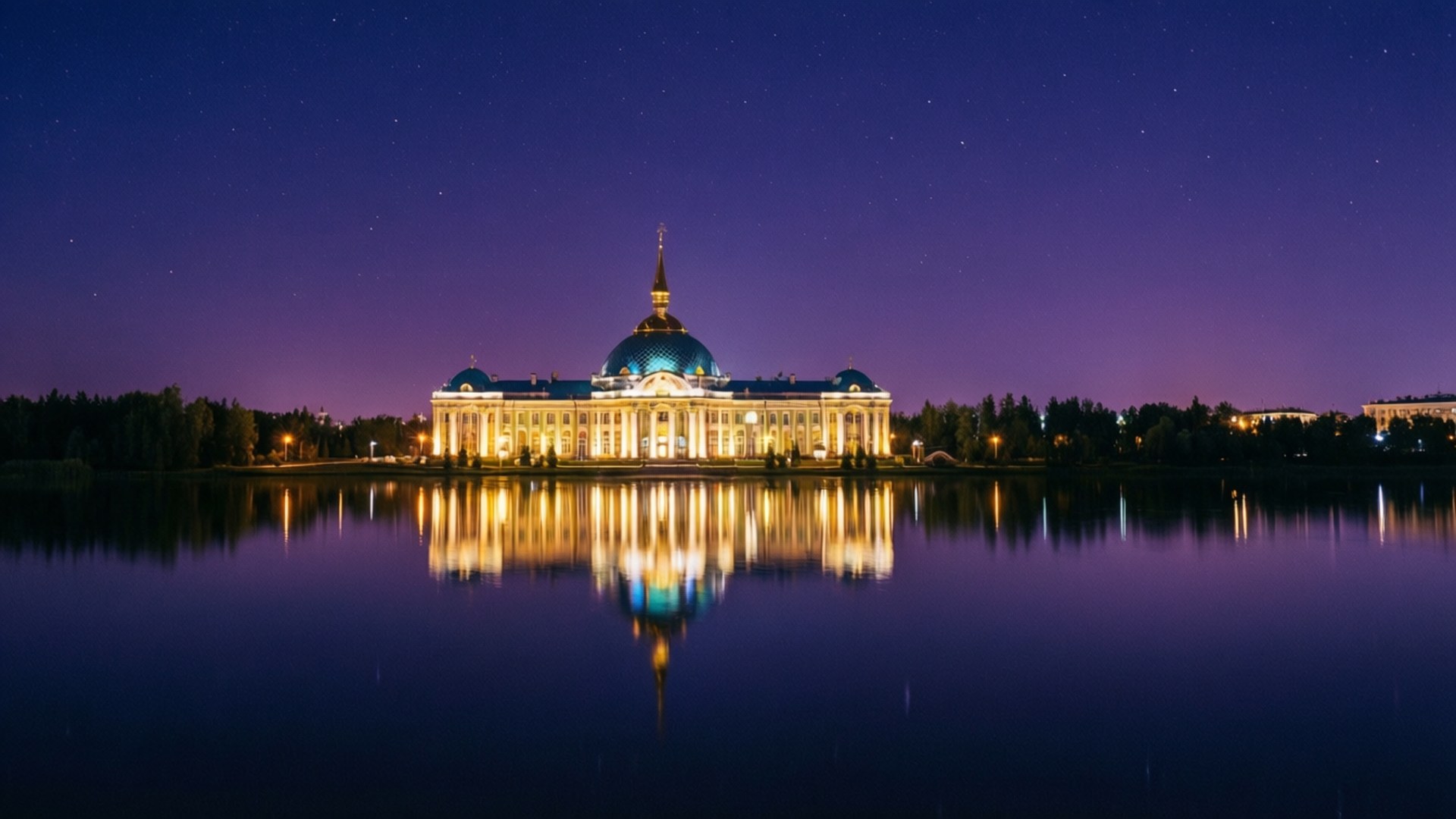 Wedding Palace Night Reflection 壁紙 — 一座宏偉的照明建築，擁有藍色圓頂和金色尖頂，在繁星點點的暮色天空下完美地倒映在平靜的水面上。
