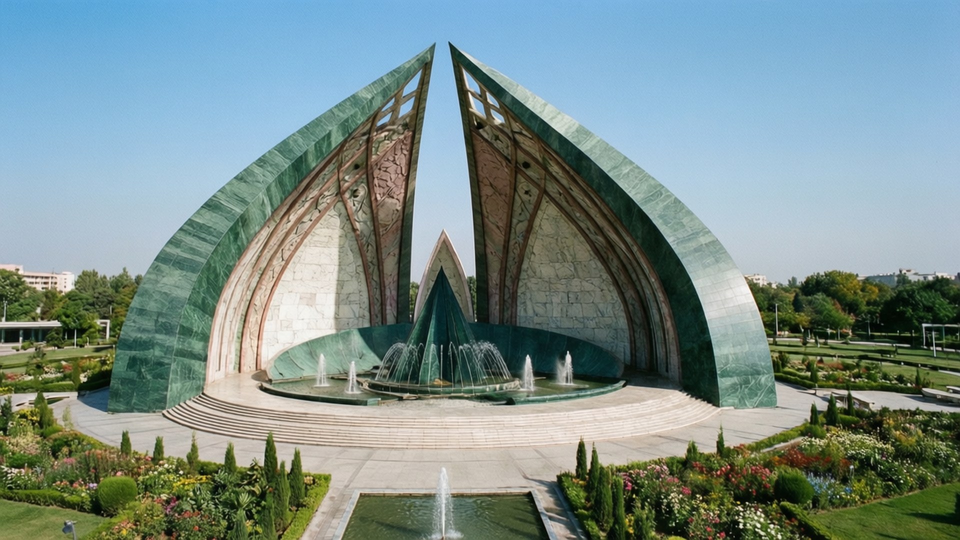 Pakistan Monument Aerial 壁紙 — 一座宏偉的紀念碑，擁有兩座高聳的綠色大理石拱門，框住了中央的噴泉，周圍是修剪整齊的花園，在清澈的藍天下。