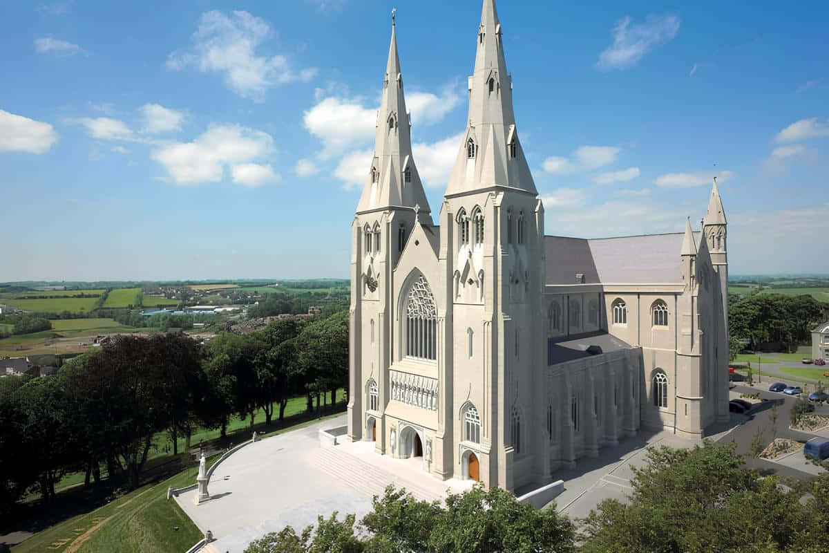 Armagh 桌布 壁紙 — 一座宏偉的石造大教堂，擁有雙塔，在點綴著蓬鬆白雲的明亮藍天下雄偉地聳立。