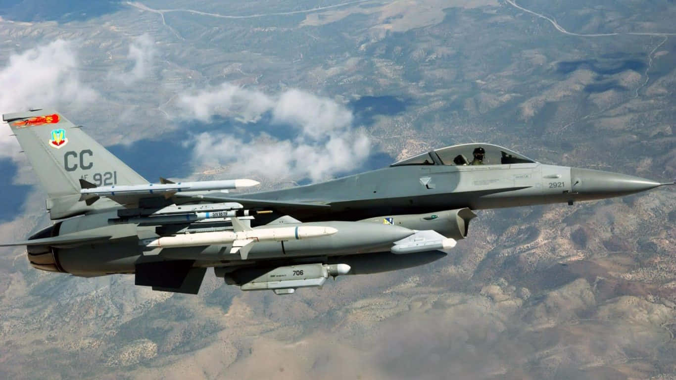 軍用戰鬥機飛越有雲的山地景觀。 — 1366X768 壁紙