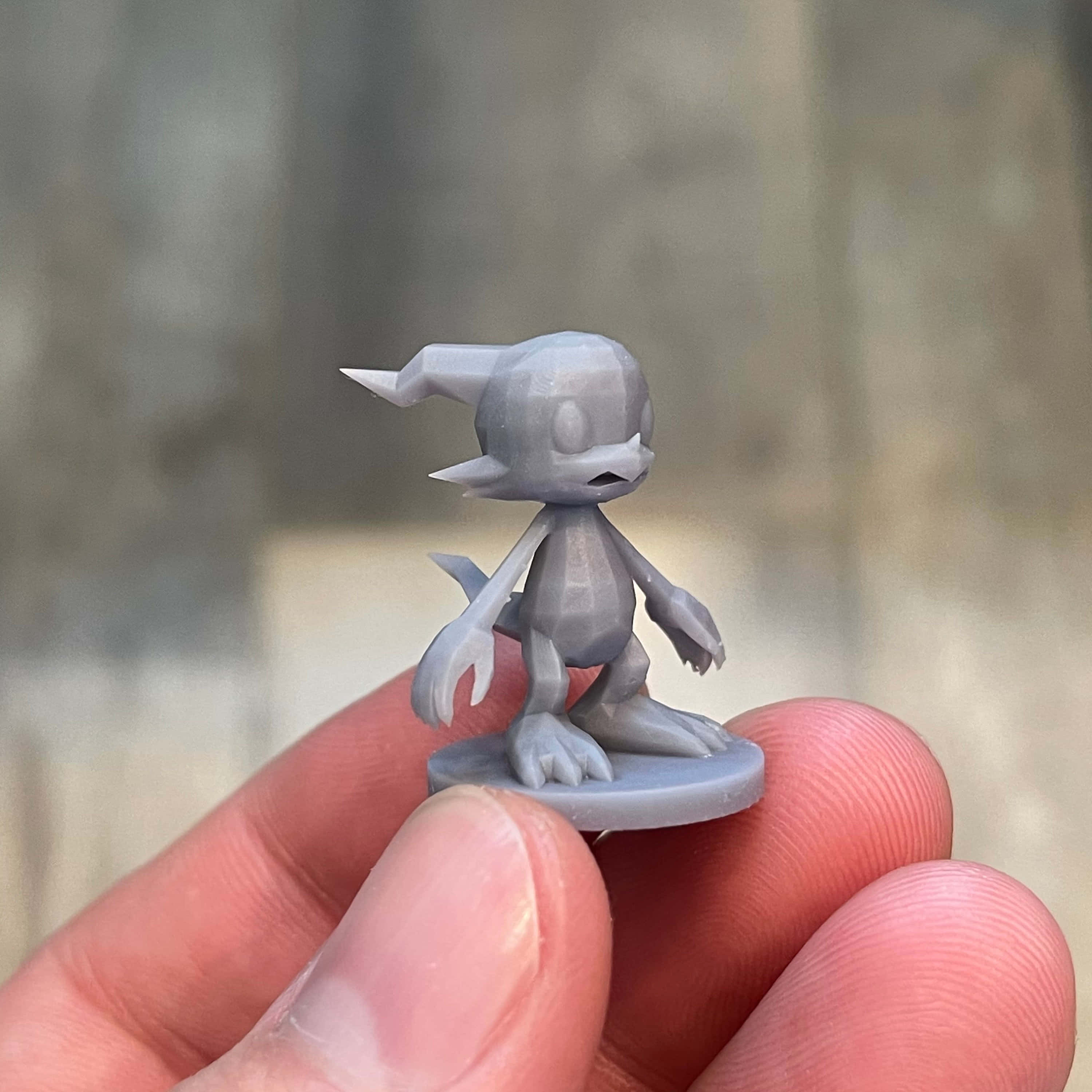 Veemon 桌布 壁紙 — 一隻手拿著一個細小灰色3D列印的風格化生物公仔，有尖耳朵和爪子。