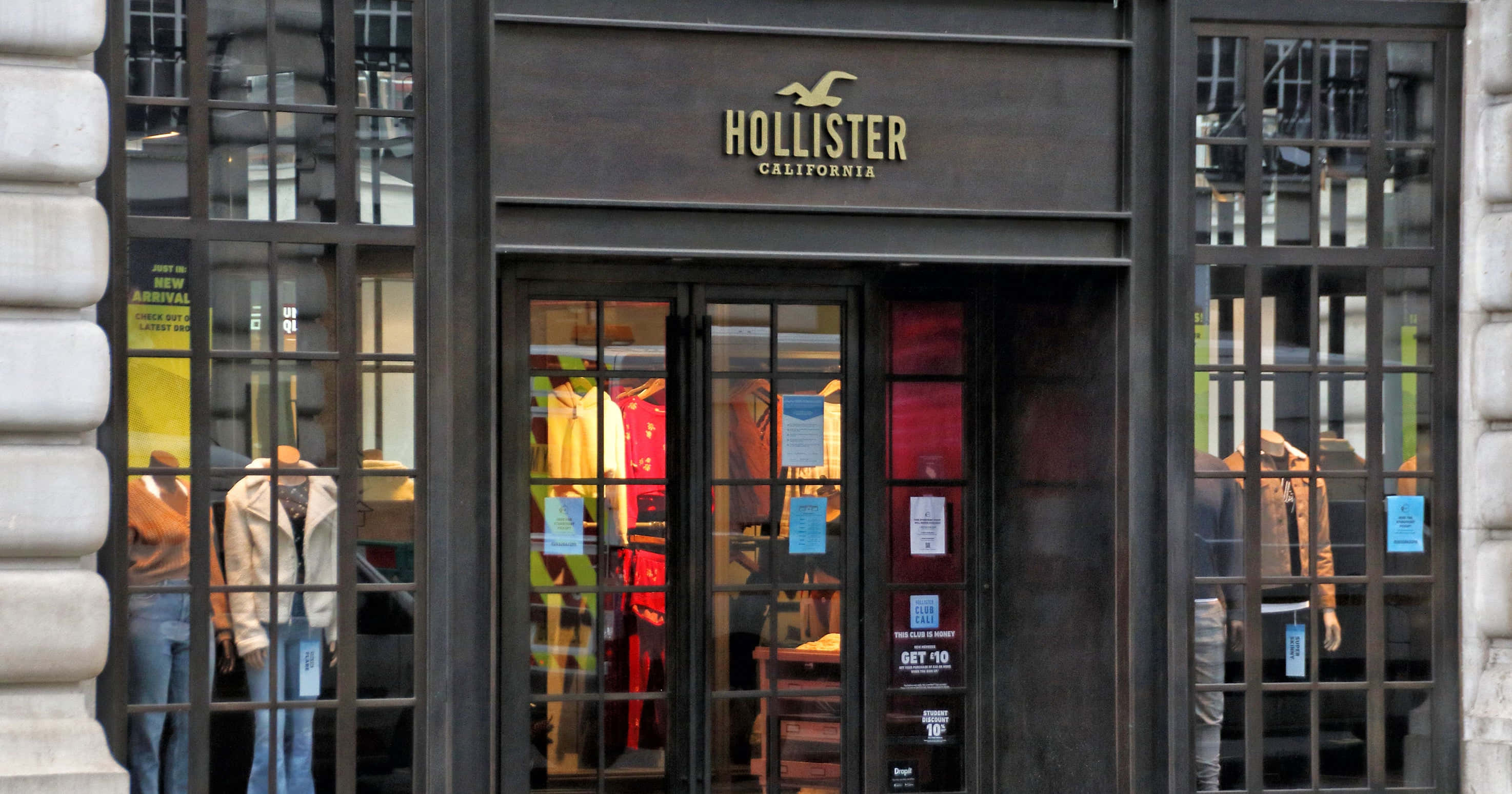 Hollister 桌布 壁紙 — Hollister California 店面正面，深色框架窗戶展示穿著休閒服裝的人體模型，室內燈光溫暖。