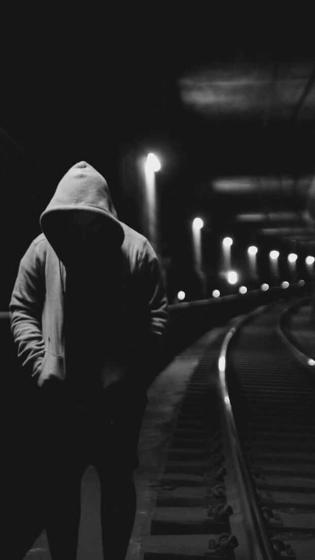 一個穿著連帽衫的人在夜間走在火車軌道上的剪影。 — 傷心 壁紙
